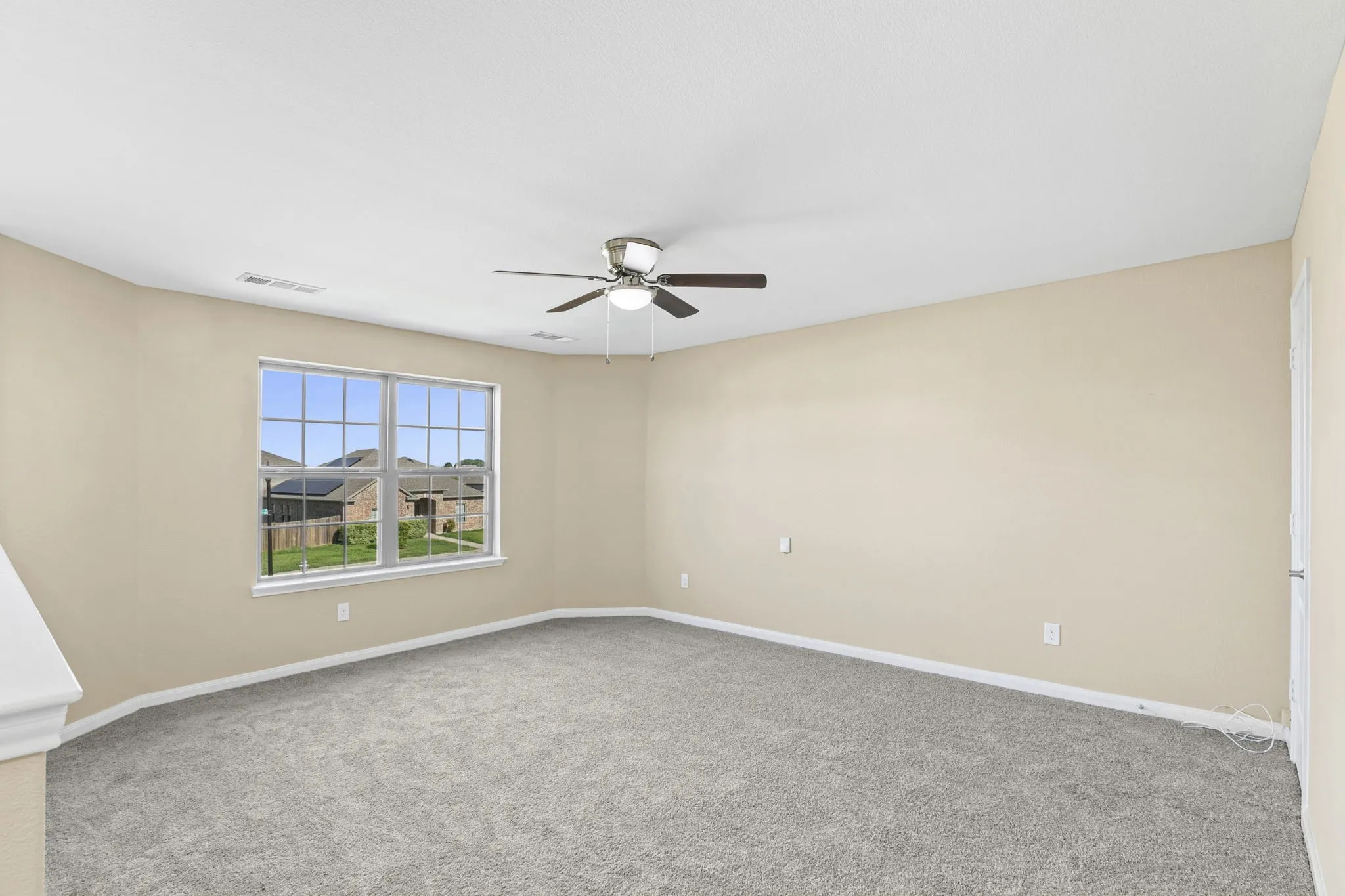 Carpeted interior space featuring neutral wall tones, a ceiling fan with integrated lighting, and a multi-pane window