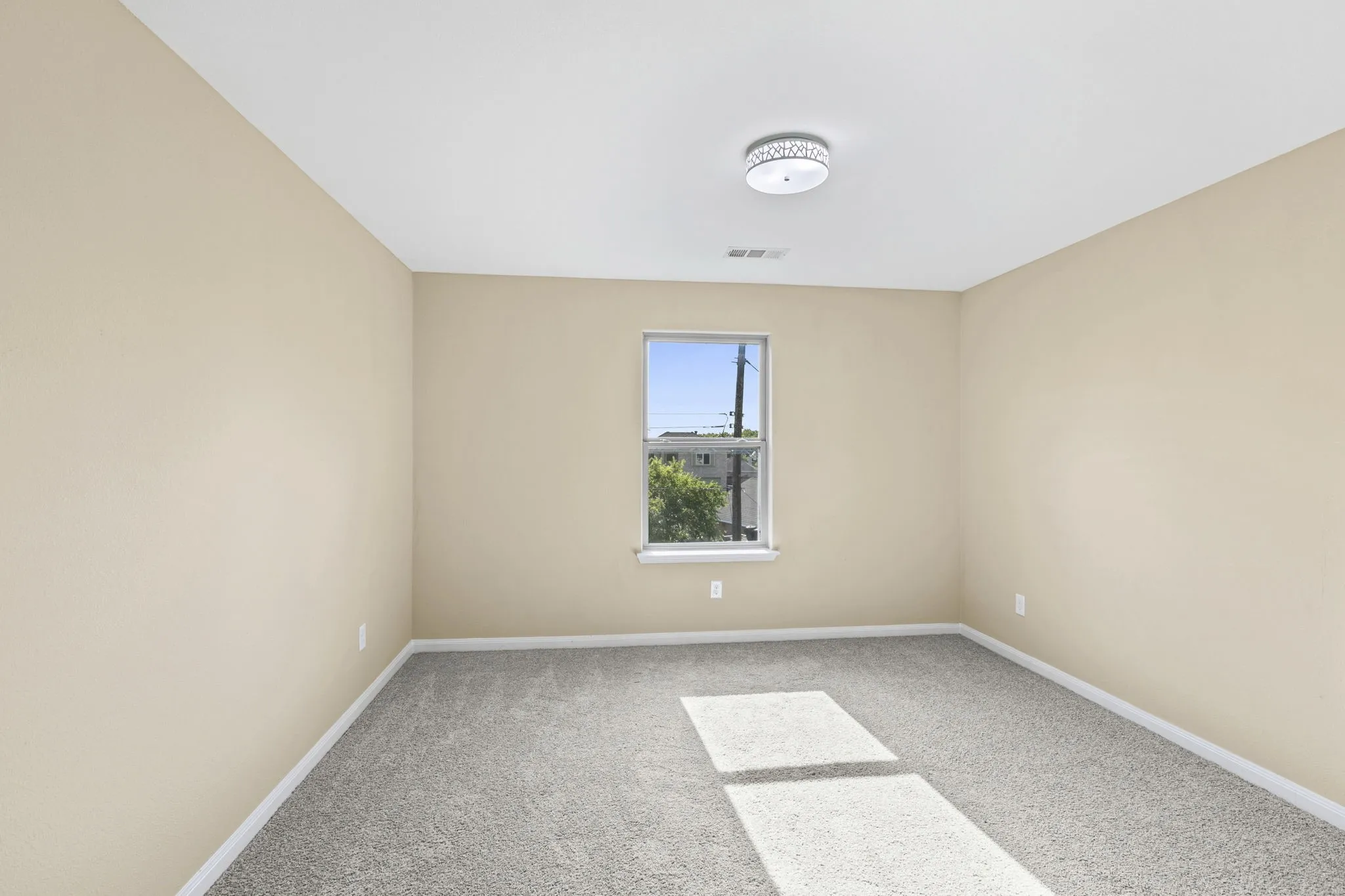 Carpeted room with a single window, neutral-toned walls, and a ceiling-mounted light fixture