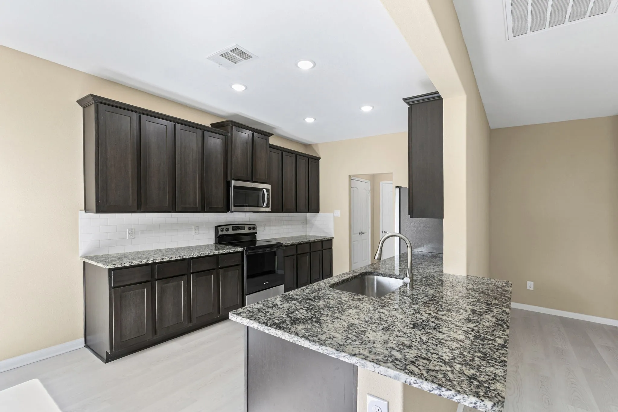 Kitchen featuring dark wood cabinetry, light-colored granite countertops, and a subway tile backsplash