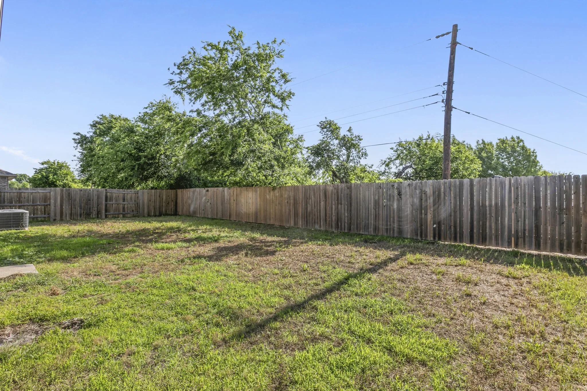 Expansive backyard space featuring a wooden privacy fence, mature trees, and a ground-mounted HVAC unit