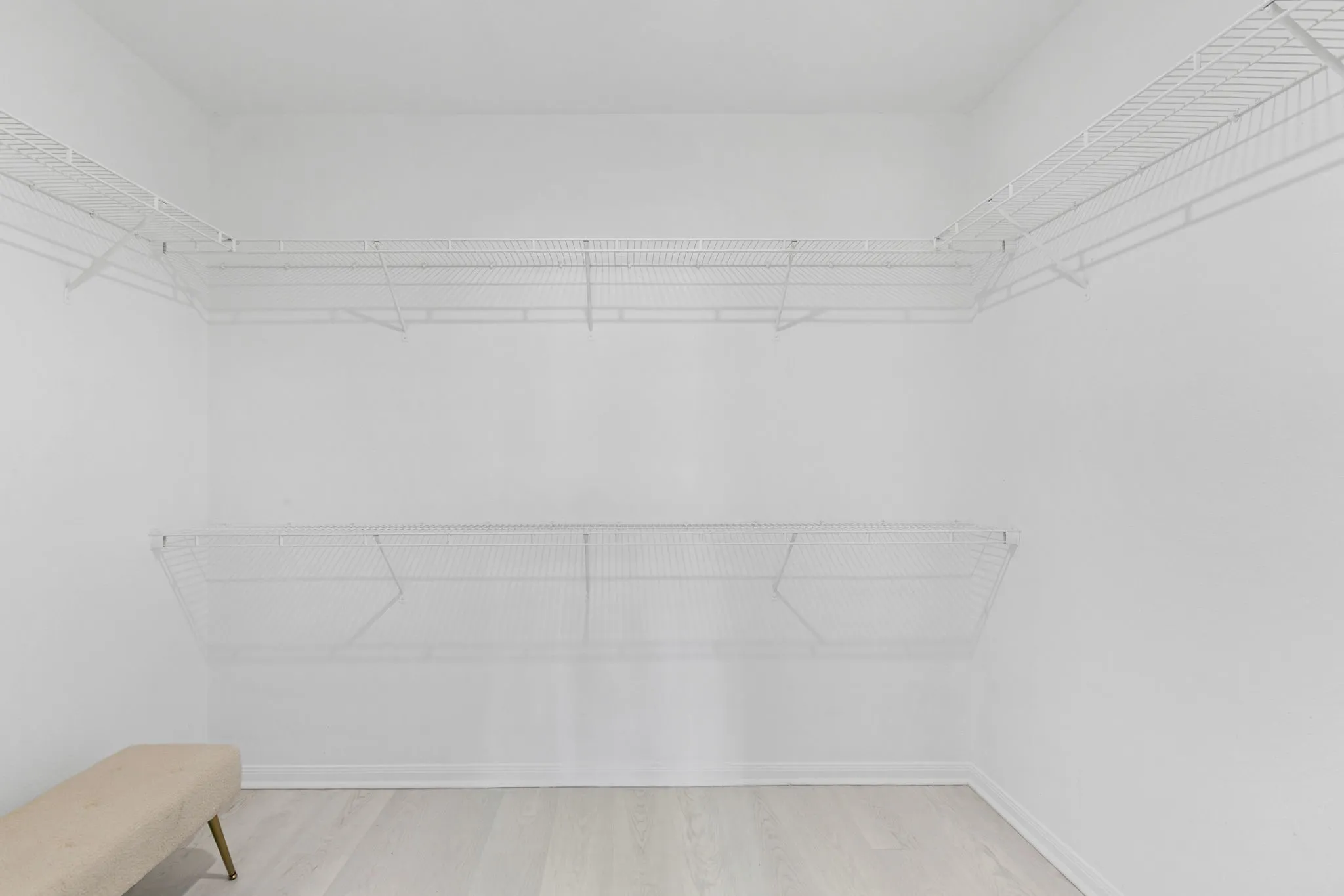 Spacious walk-in closet featuring white wire shelving, light wood-finish flooring, and white baseboards