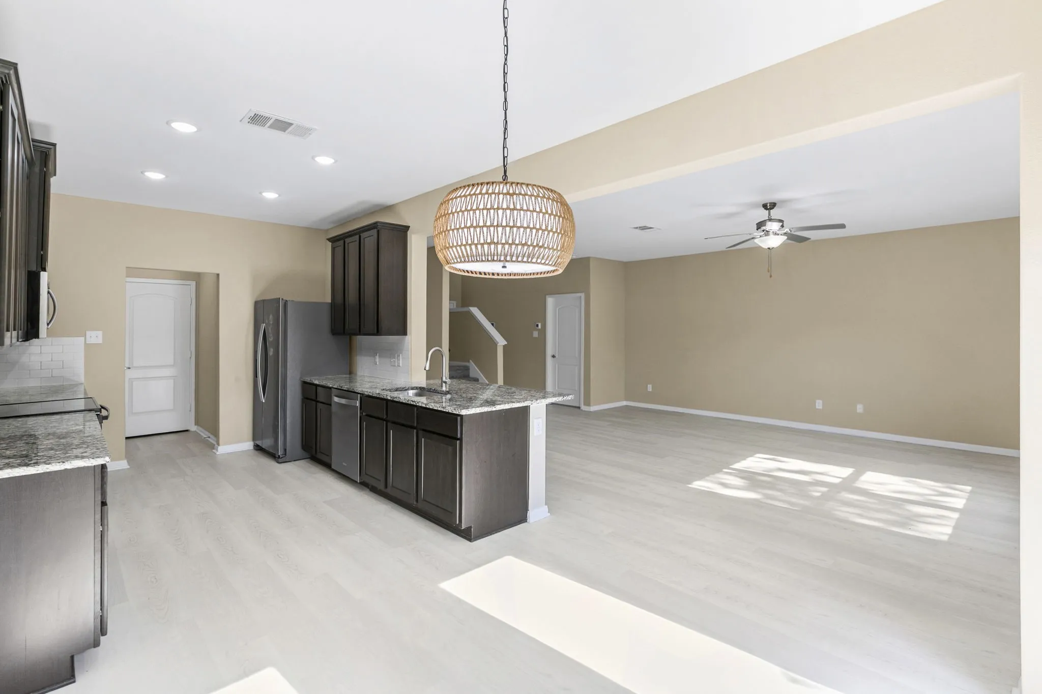 Open-concept kitchen featuring dark wood cabinetry, light wood-finish flooring, and a kitchen island with sink