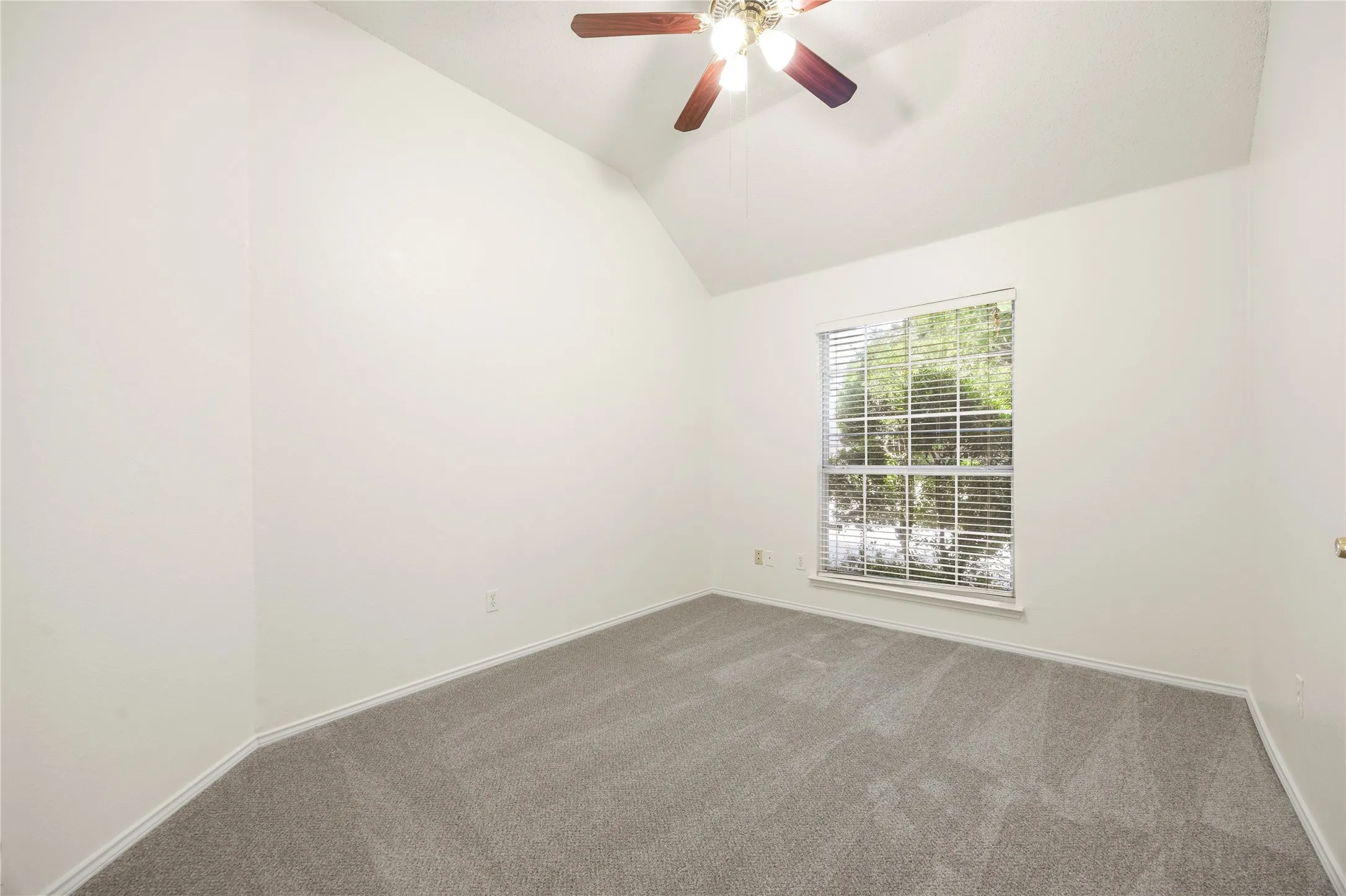 Vaulted ceiling room featuring light gray carpeting, a window with blinds, and a ceiling fan with light fixture