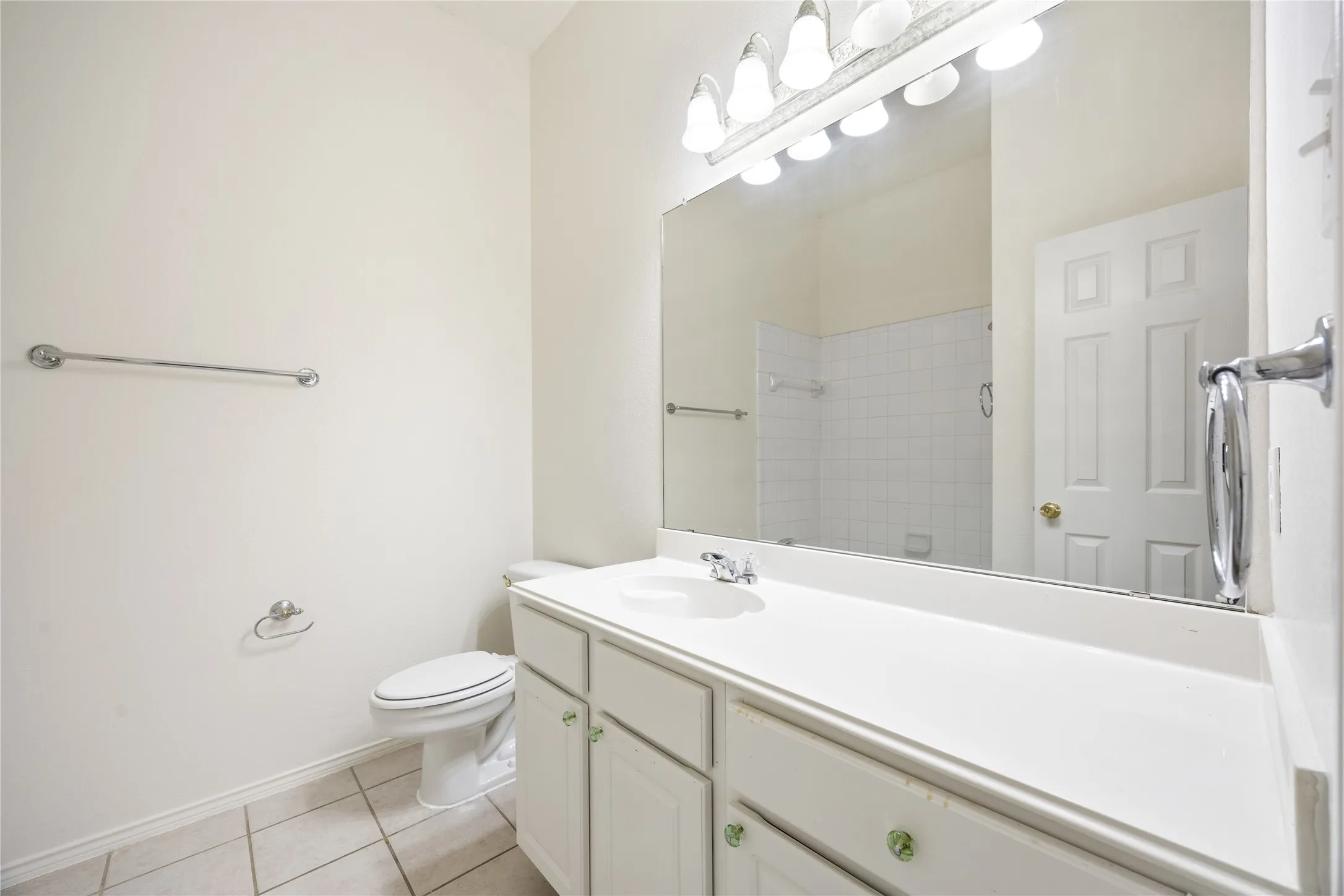 Bathroom featuring a single vanity with a white countertop and base cabinetry, chrome fixtures, an overhead light bar, and tiled flooring