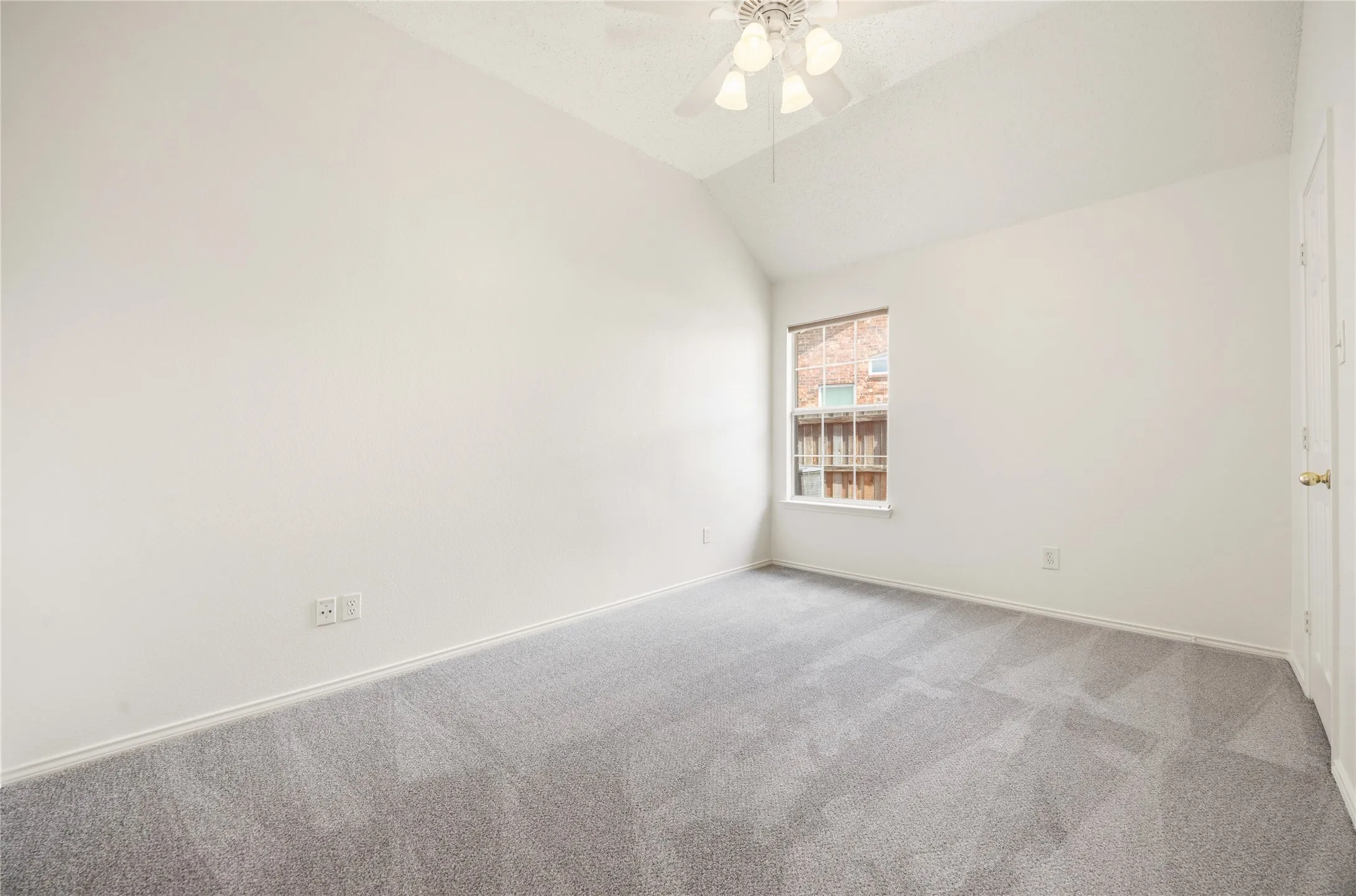 Spacious room featuring vaulted ceilings, light gray carpeting, a multi-pane window, and a ceiling fan with integrated lighting