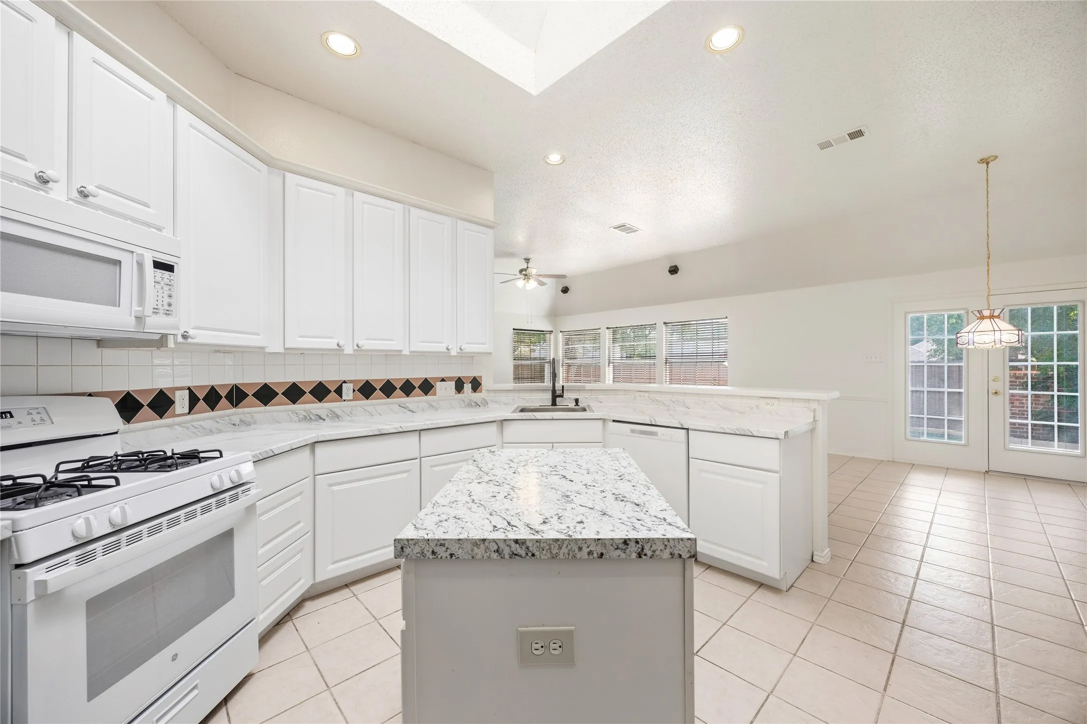 Kitchen featuring white cabinetry, white appliances, speckled countertops, a skylight, and tile flooring