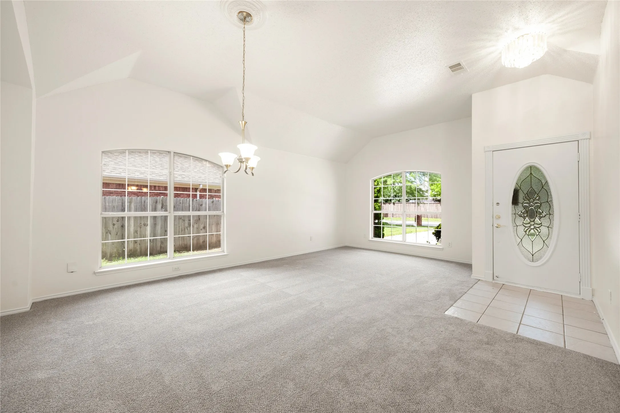 Spacious room featuring vaulted ceilings, light gray carpeting, and two arched windows
