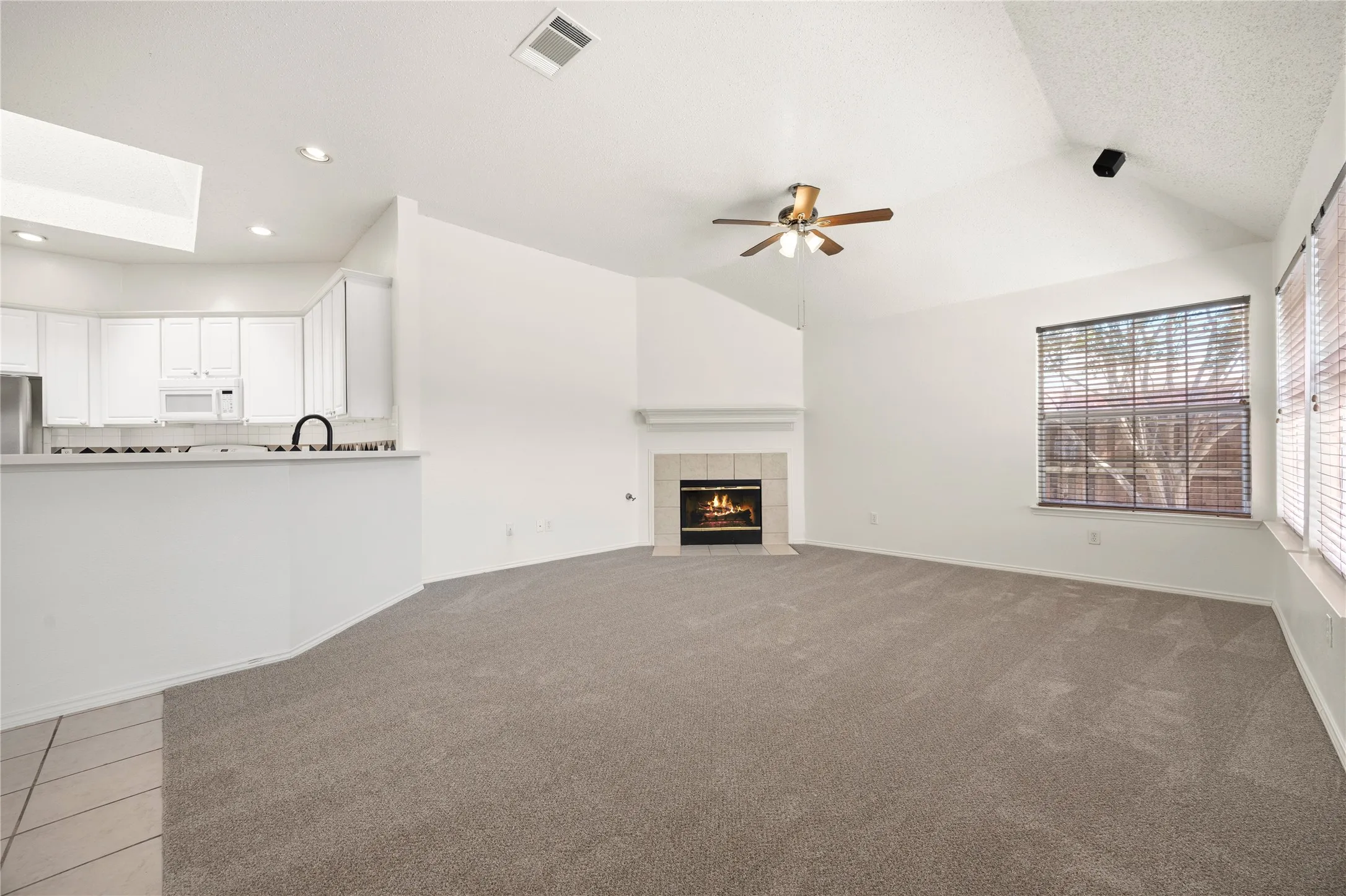 Spacious living area featuring a vaulted ceiling, ceiling fan, and a fireplace with a tile surround