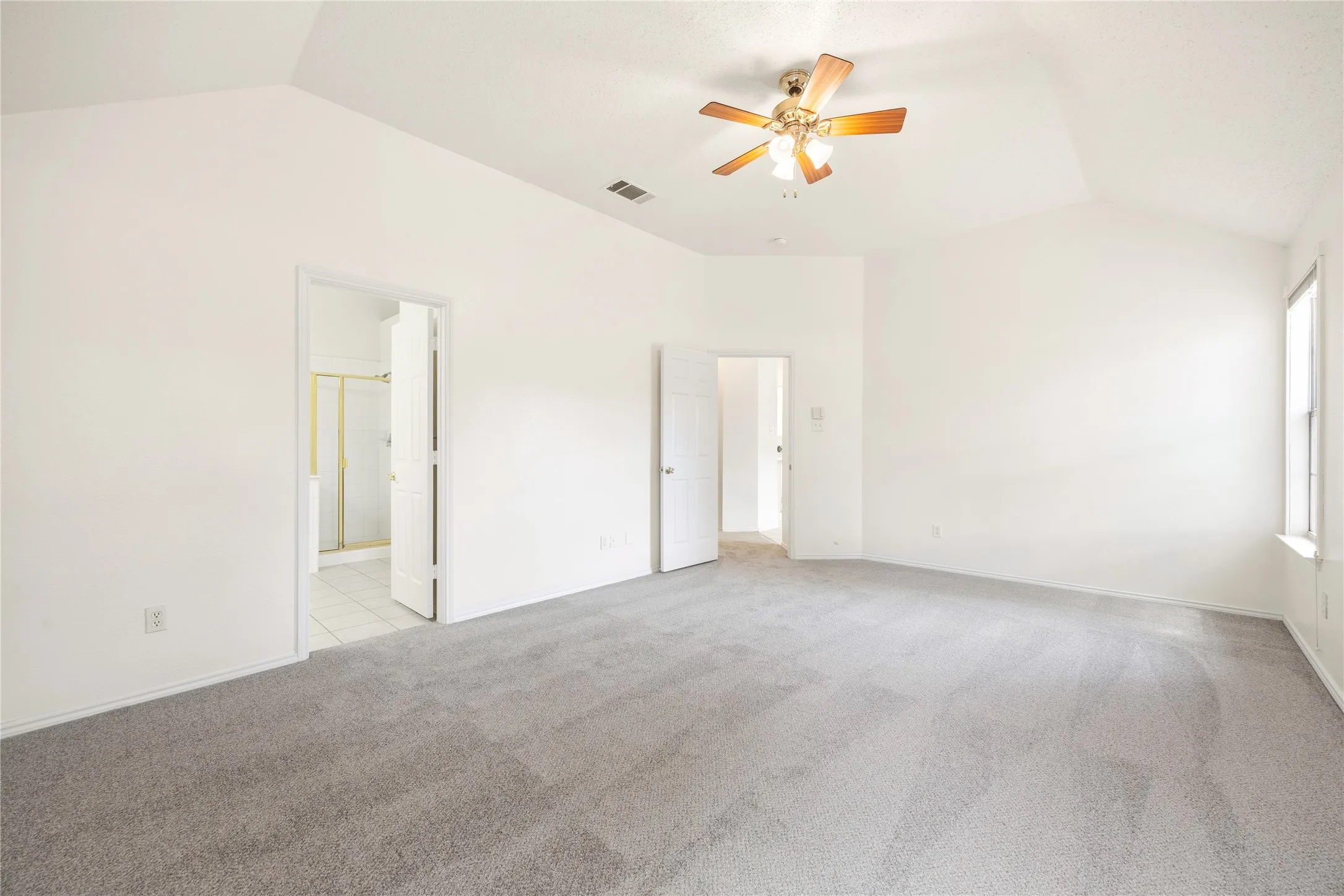 Spacious room featuring vaulted ceilings, neutral-toned carpeting, and a ceiling fan with integrated lighting