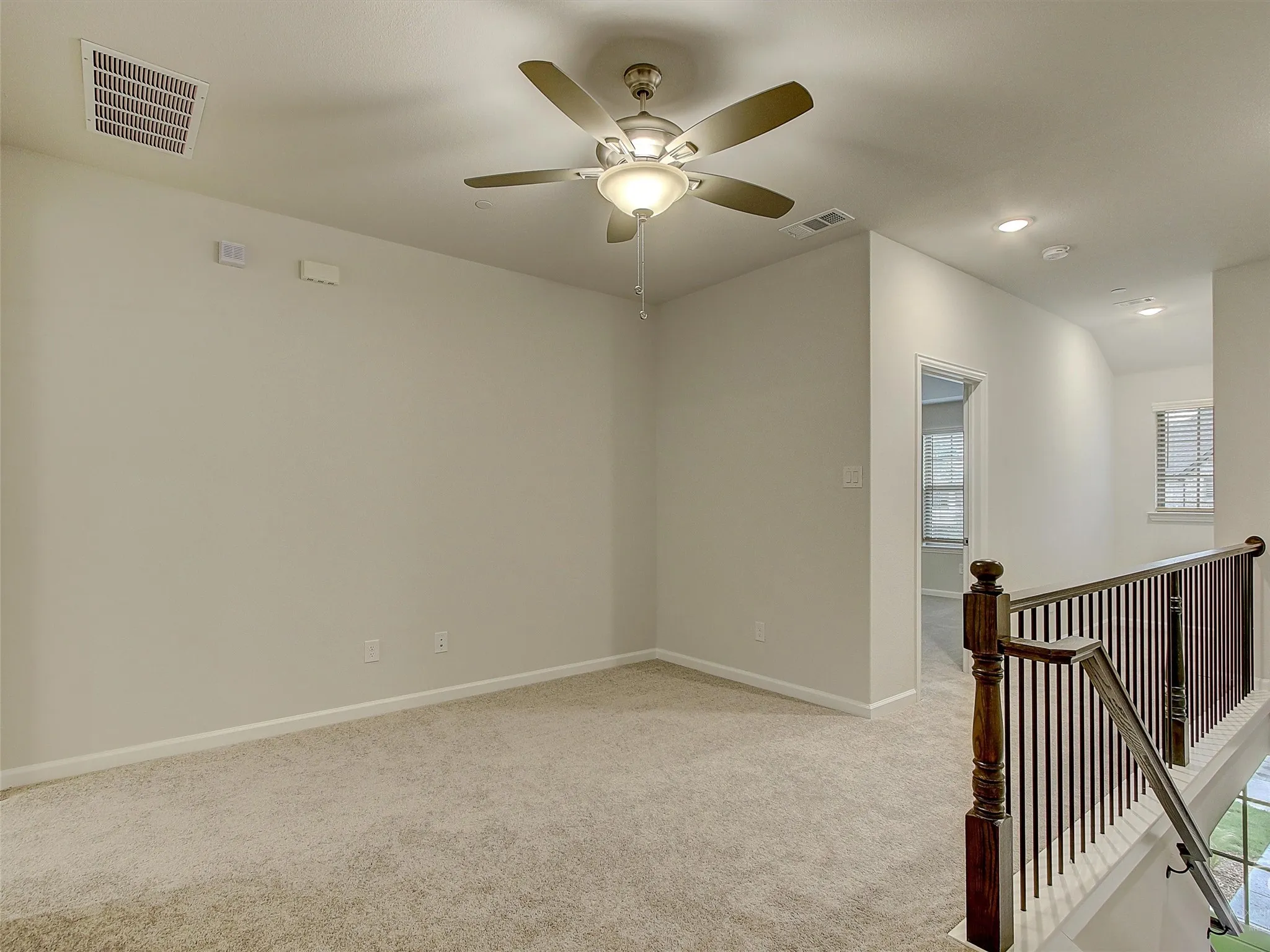 Carpeted loft area featuring a ceiling fan with light fixture, recessed lighting, and a dark wood-finish staircase railing