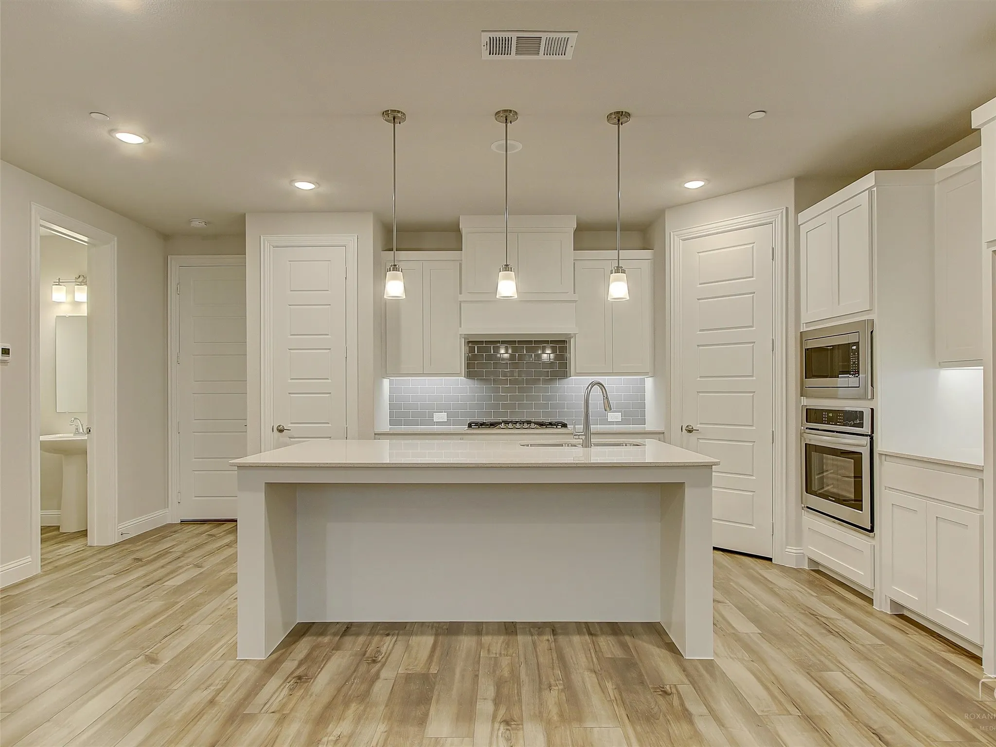 Contemporary kitchen featuring a large central island, pendant lighting, stainless steel double ovens, a built-in microwave, and wood-finish flooring