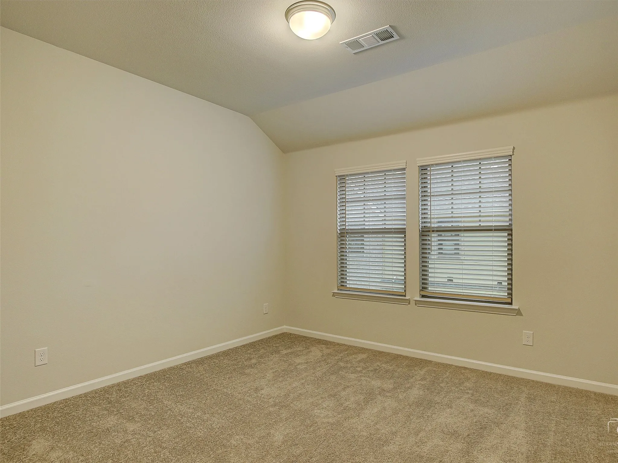 Carpeted room featuring two windows with horizontal blinds, light beige walls, a vaulted ceiling, and a flush-mount ceiling light fixture