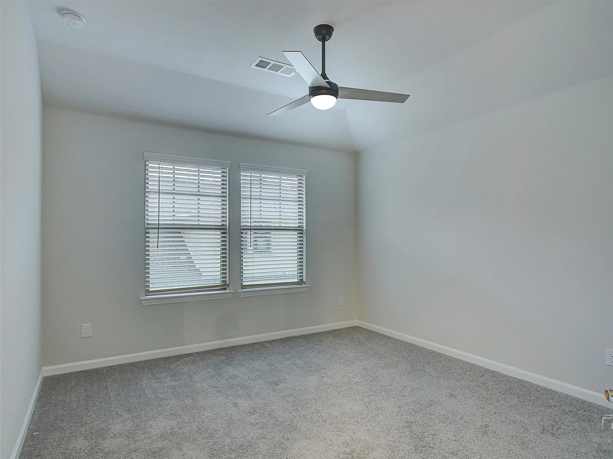 Carpeted room featuring two windows with horizontal blinds, a ceiling fan with integrated lighting, and neutral wall paint