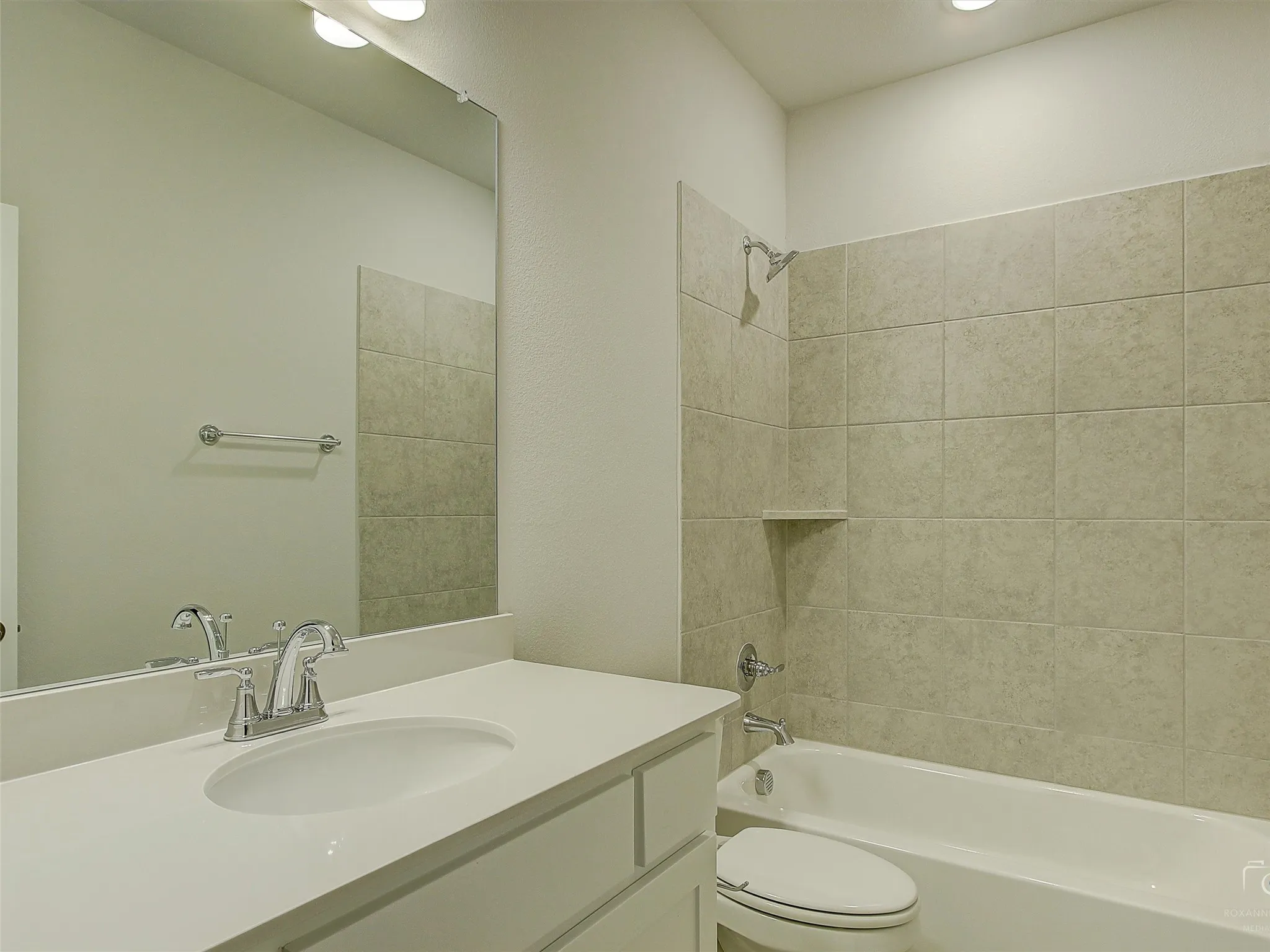 Bathroom featuring a single vanity with an integrated sink, polished chrome faucet, a large frameless mirror, and a tub-shower combination with tiled surround