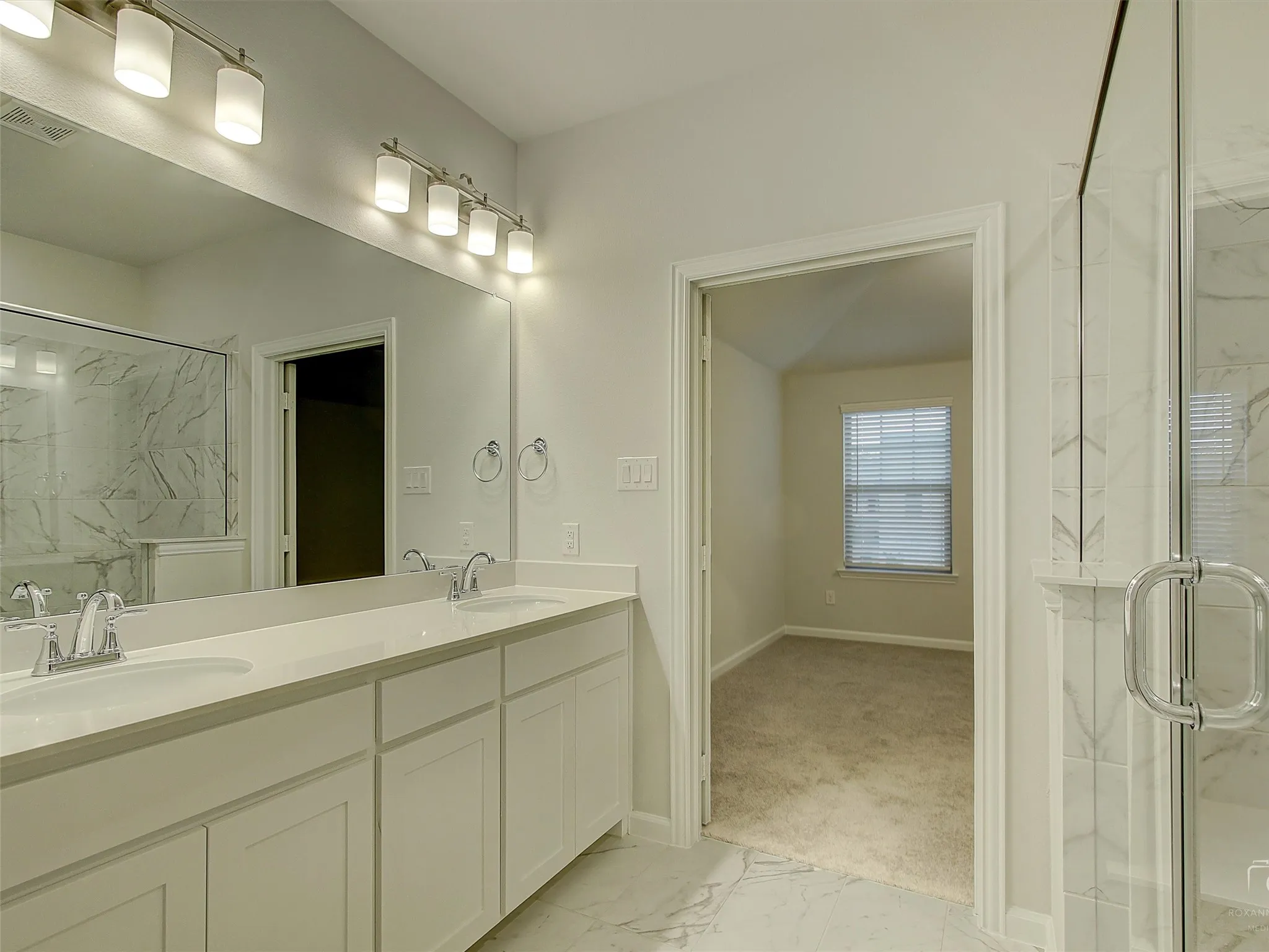 Bathroom featuring a double vanity with white cabinetry and a light-toned countertop, a large wall-mounted mirror, and a glass-enclosed shower with tiled walls