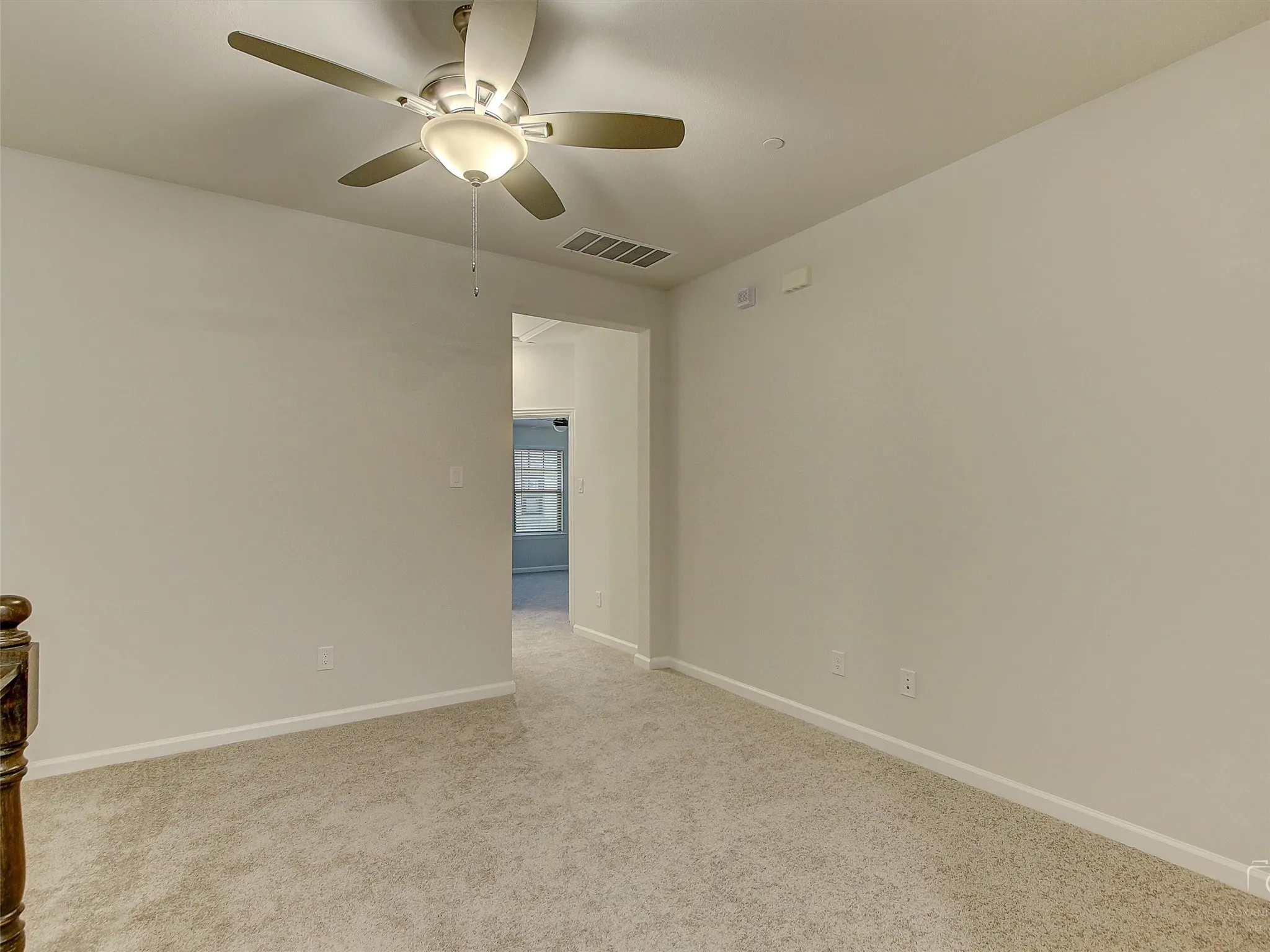 Spacious room featuring neutral carpeting, light-toned walls, and a ceiling fan with integrated lighting