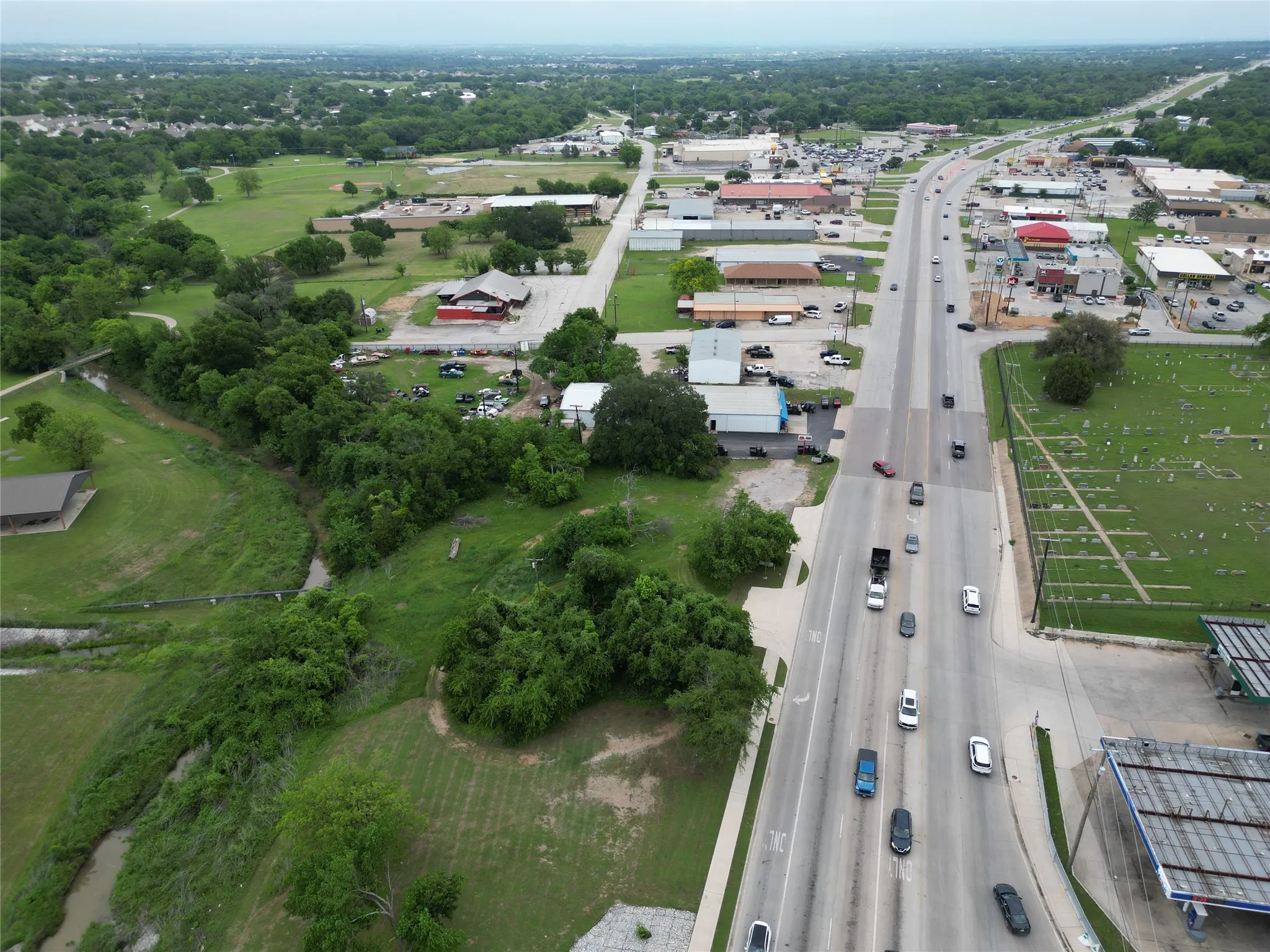 Aerial perspective highlighting a multi-lane roadway with active traffic, adjacent commercial structures, and extensive green spaces