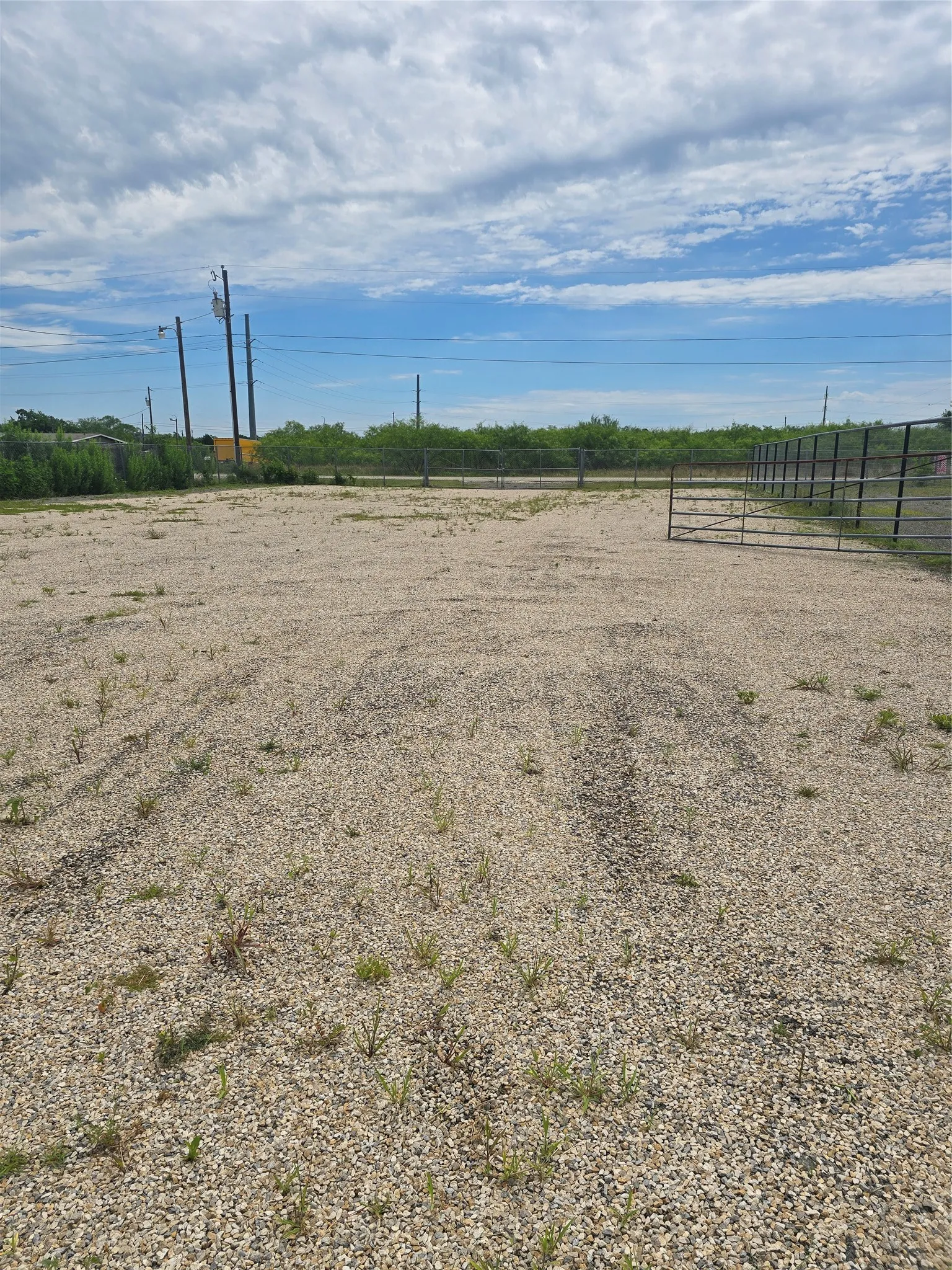 Expansive gravel lot featuring a metal gate and partial fencing