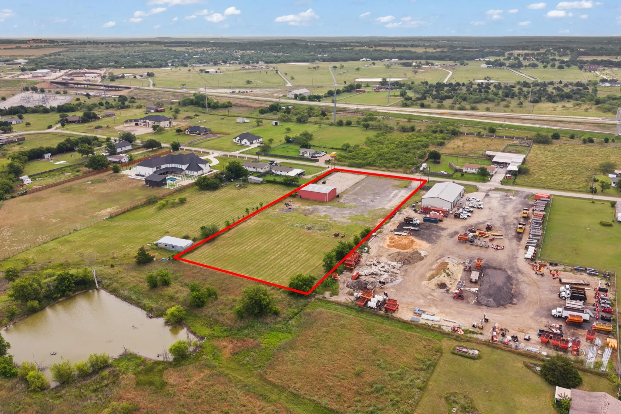 Expansive land parcel featuring a red barn structure, paved area, and surrounding green space