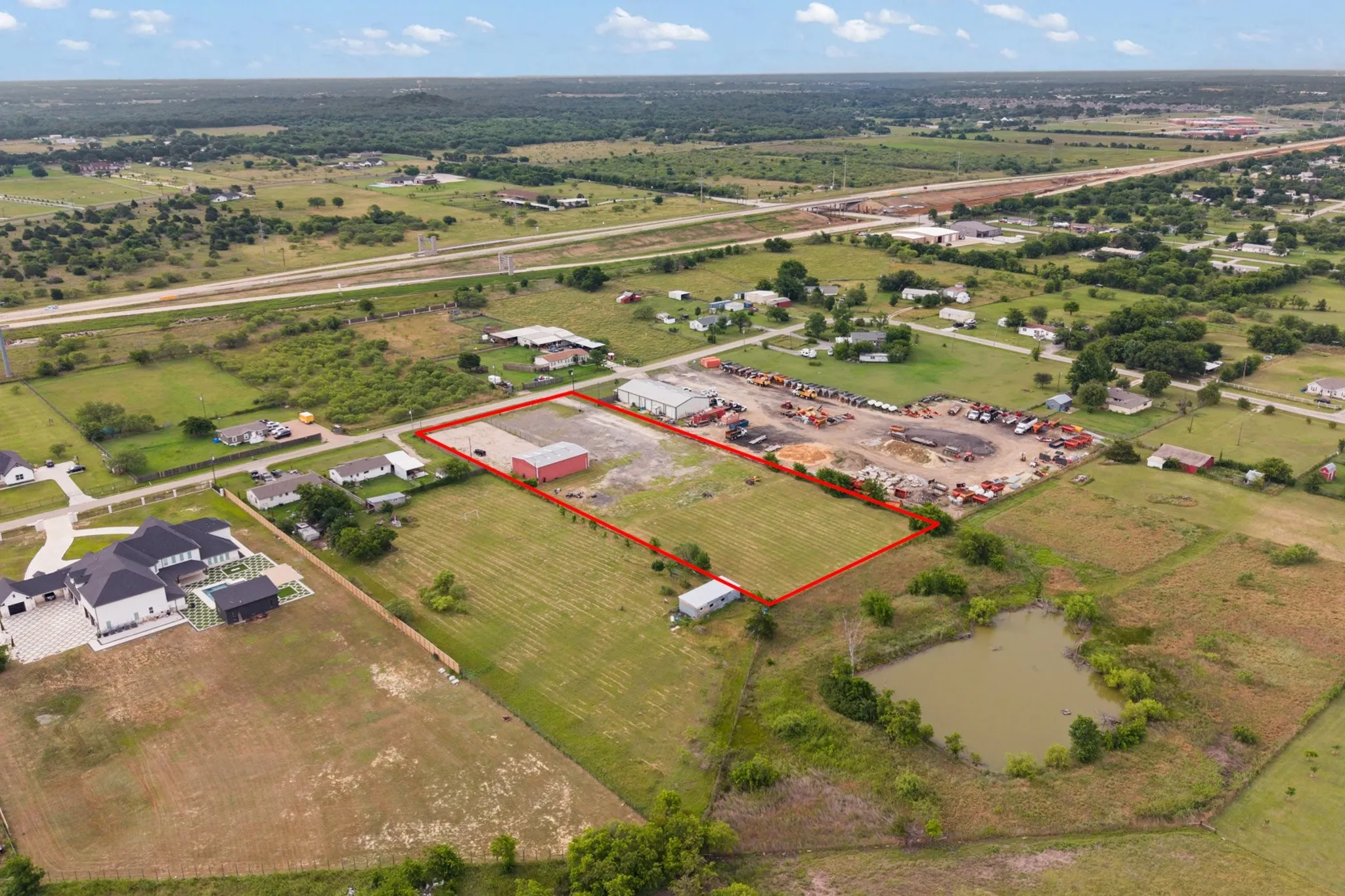 Expansive land parcel featuring an established commercial building, open land area, and a natural pond