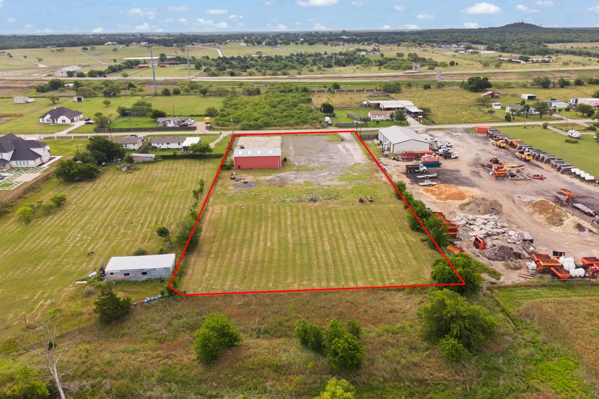 Expansive property featuring a red industrial building with a light-colored roof, a second white industrial building, and a large open field