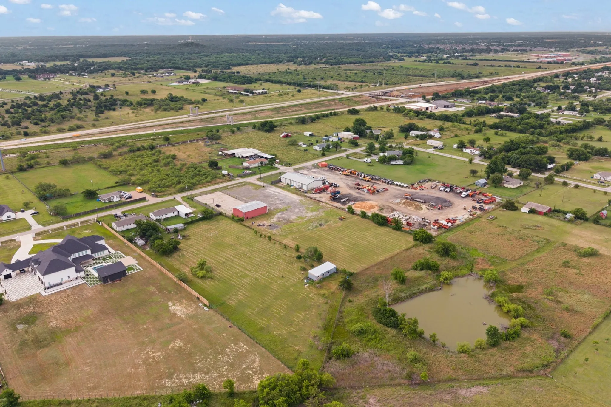 Expansive land parcel featuring a natural pond, open fields, and proximity to highway infrastructure