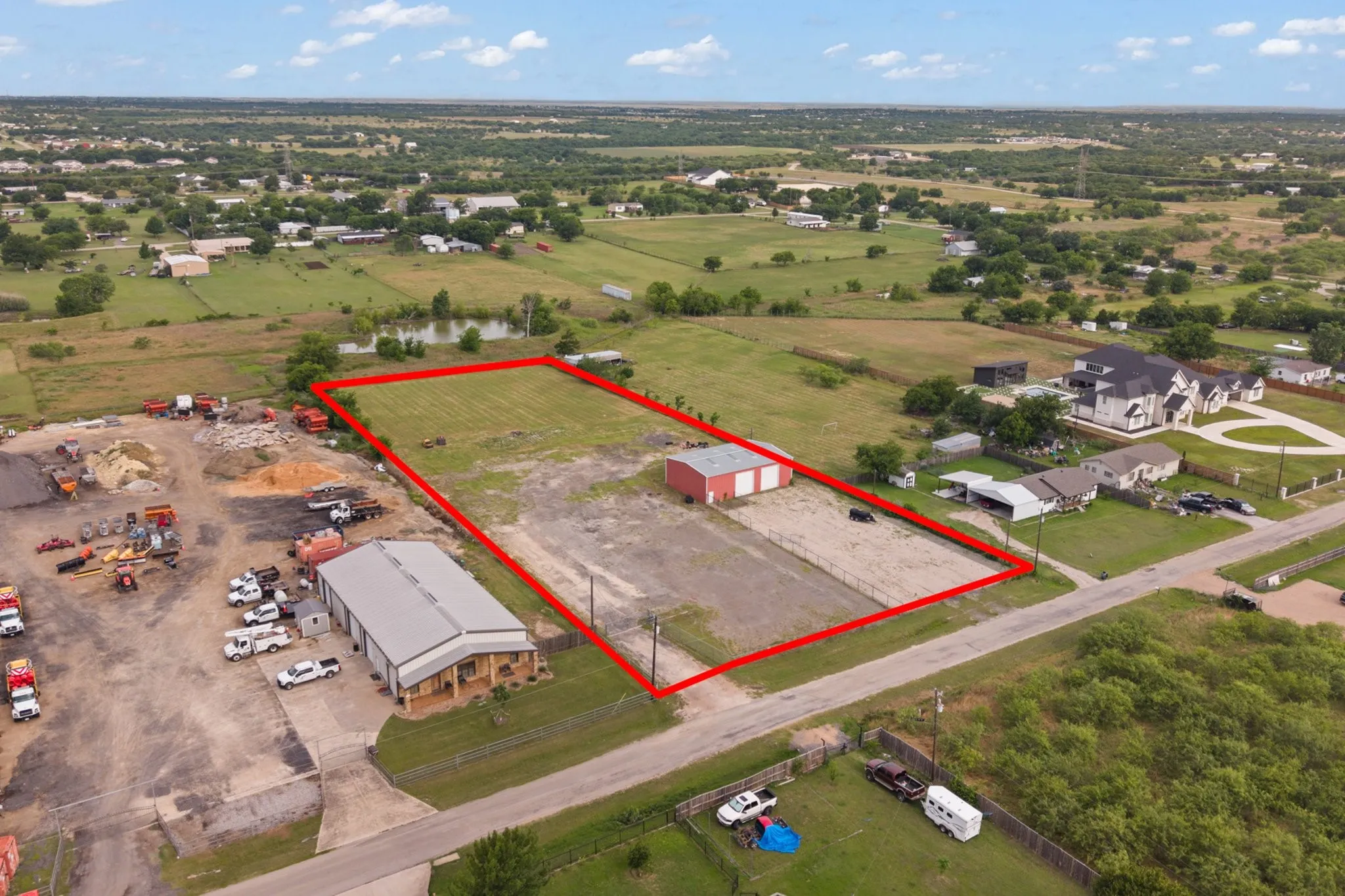 Expansive lot featuring a red-roofed building, gravel and grass areas, and a paved road frontage