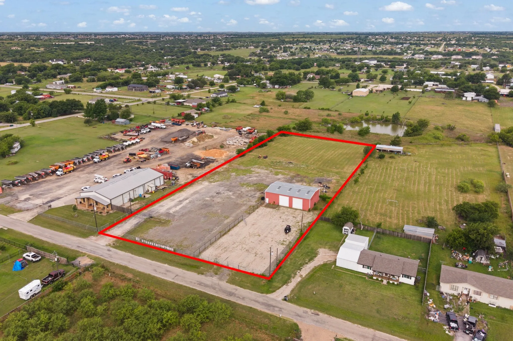 Expansive commercial property featuring a large metal building with a brick facade, a separate red barn structure, and substantial open land