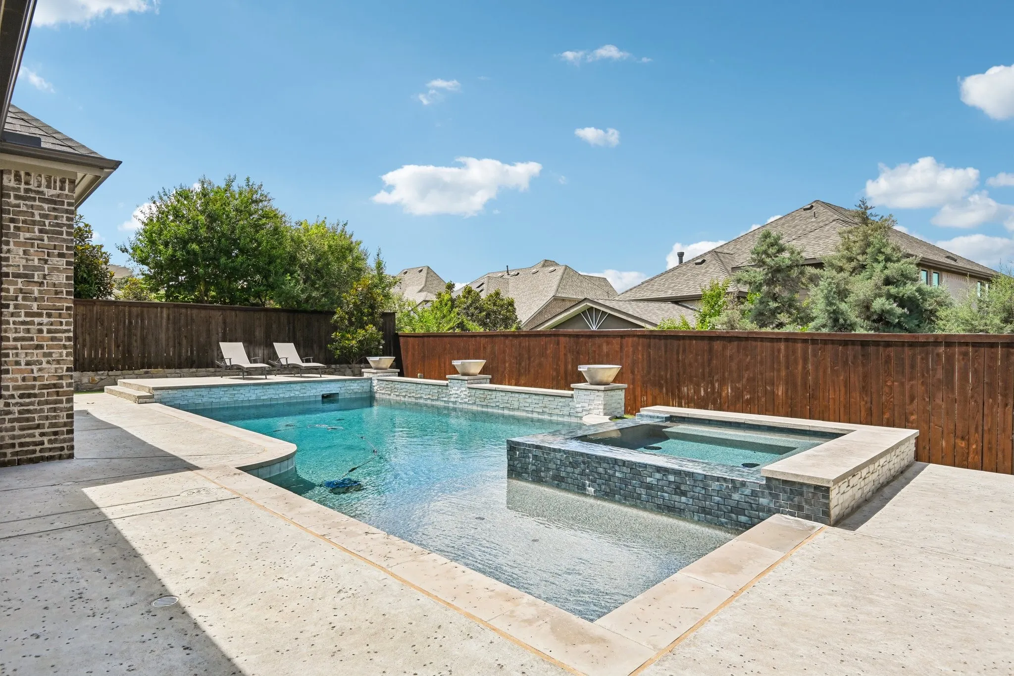 Expansive backyard featuring a large swimming pool, integrated spa, surrounding concrete patio, and a wood privacy fence