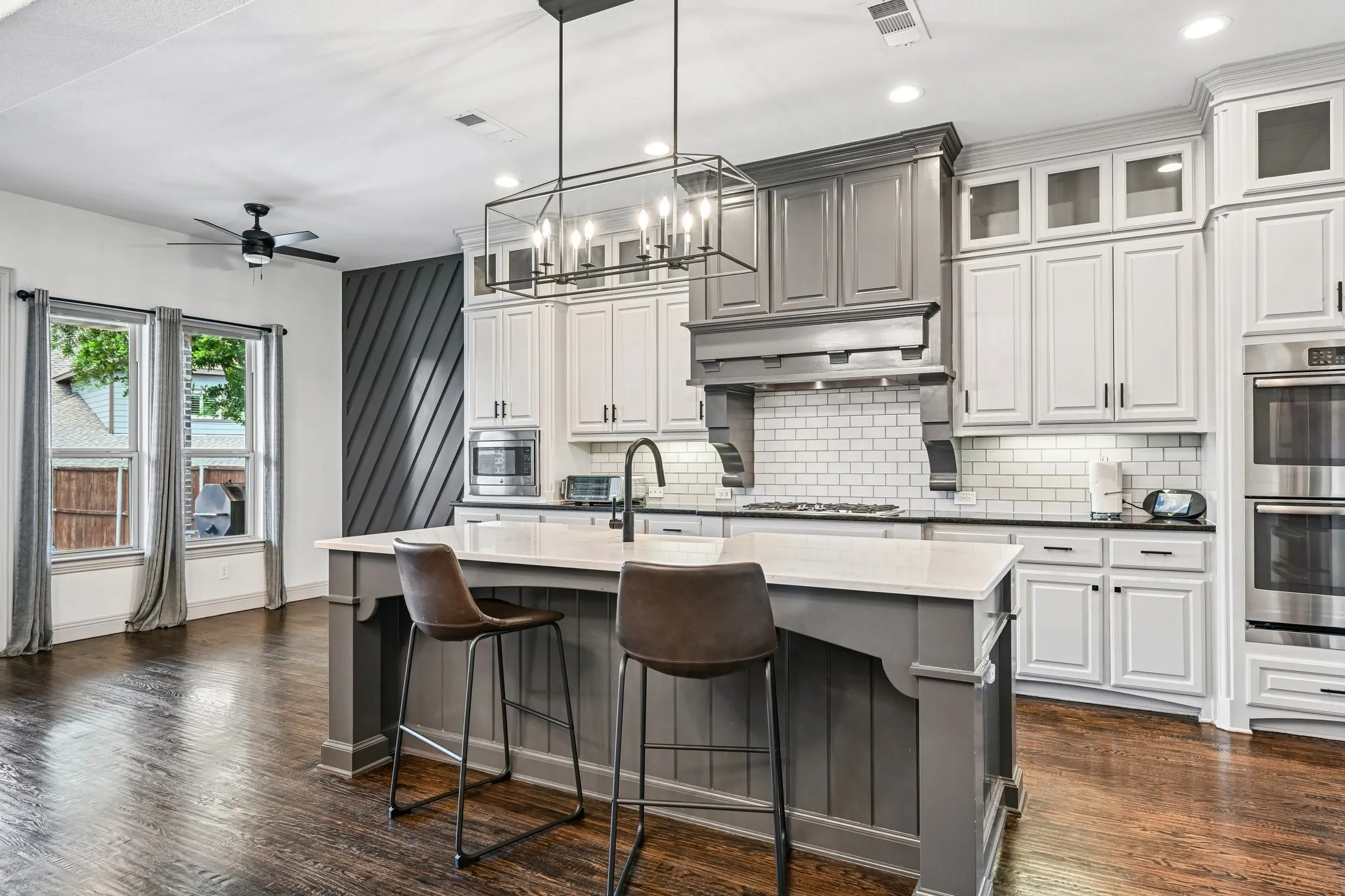 Gourmet kitchen featuring a large central island with seating, a subway tile backsplash, stainless steel double ovens, custom cabinetry in two-tone finishes, and dark wood-finish flooring