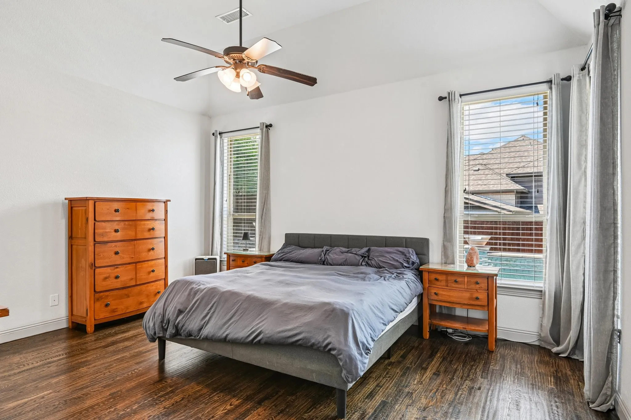 Vaulted ceiling with a flush-mount fan-light fixture, two vertical windows with blinds, and wood-finish flooring