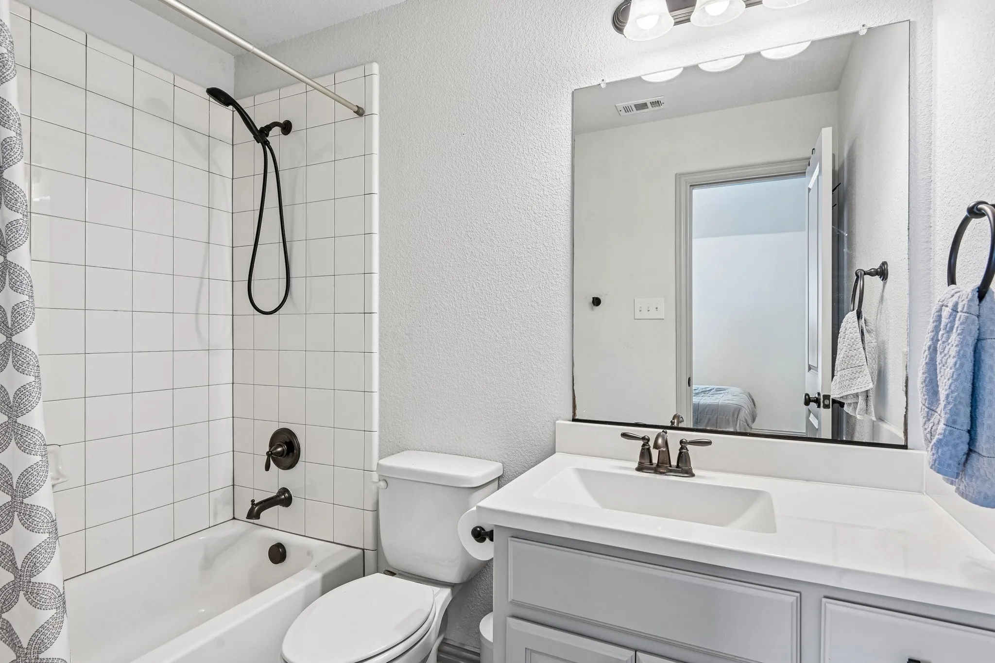Bathroom featuring a white subway tile shower surround with dark bronze fixtures, a white bathtub, a toilet, a vanity with a white countertop, and a mirror with overhead lighting