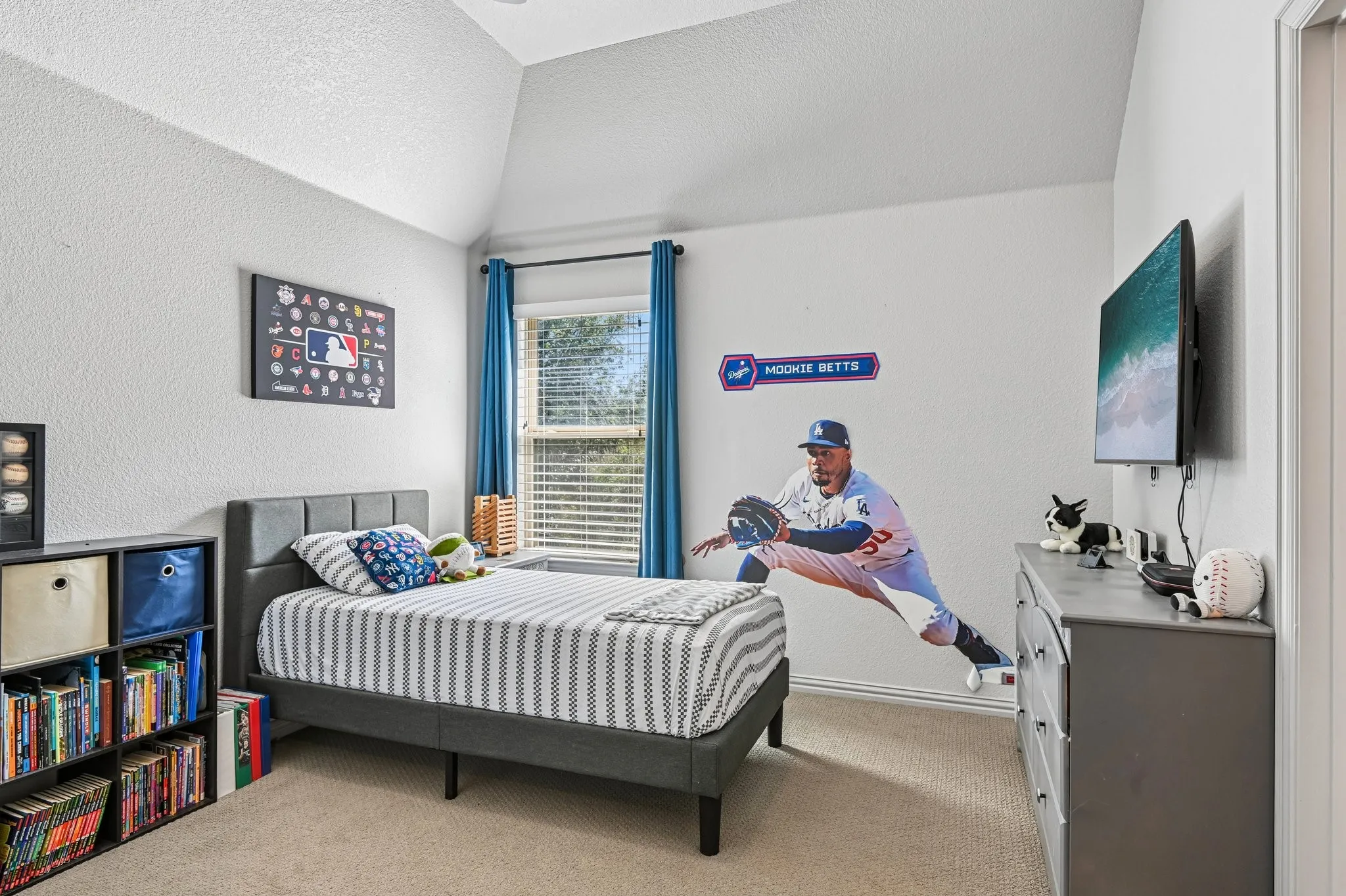 Carpeted bedroom featuring a vaulted ceiling, a window with blinds and blue curtains, and a built-in shelving unit with storage cubes