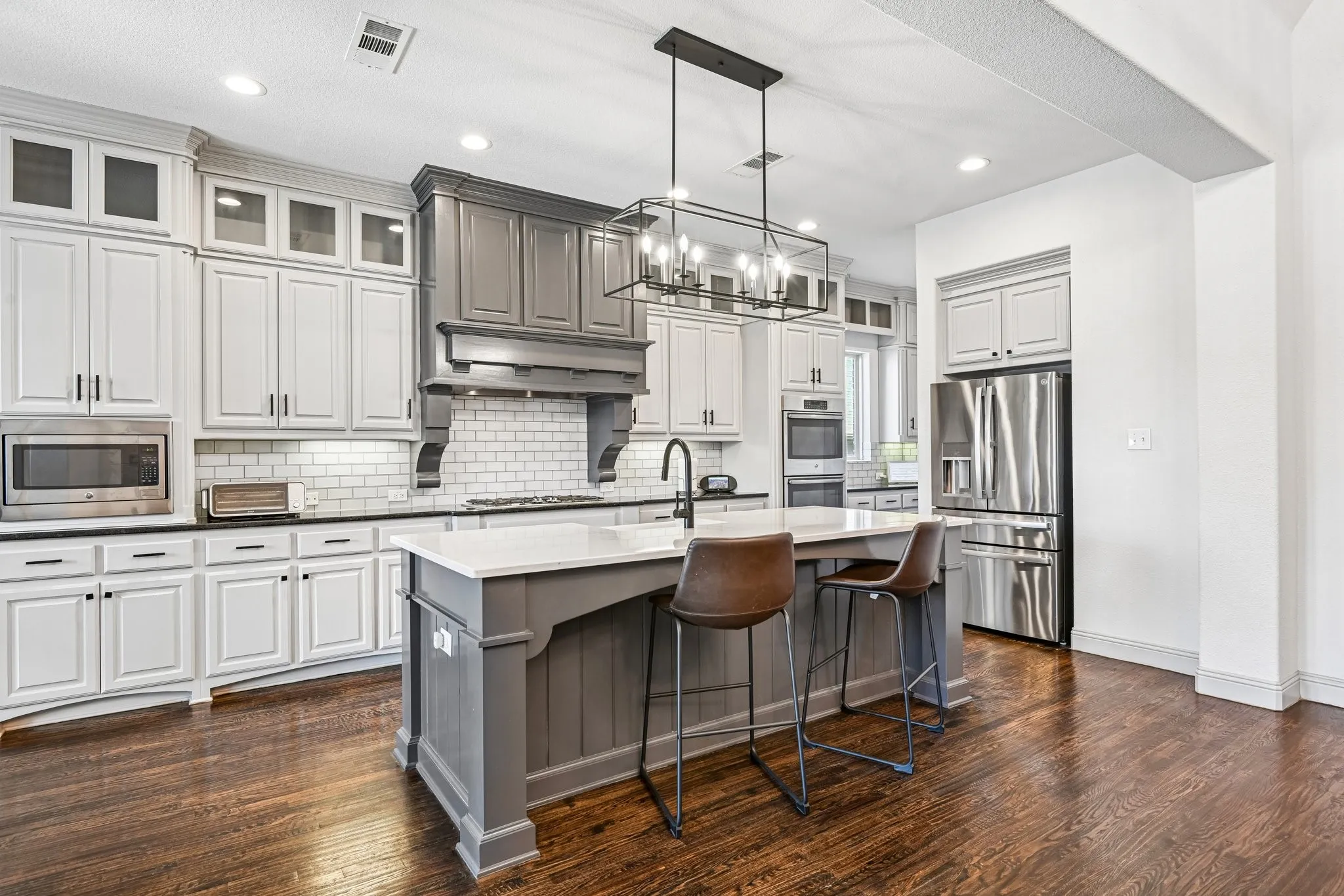 Gourmet kitchen featuring a substantial island with seating, a white subway tile backsplash, stainless steel appliances, and wood-finish flooring