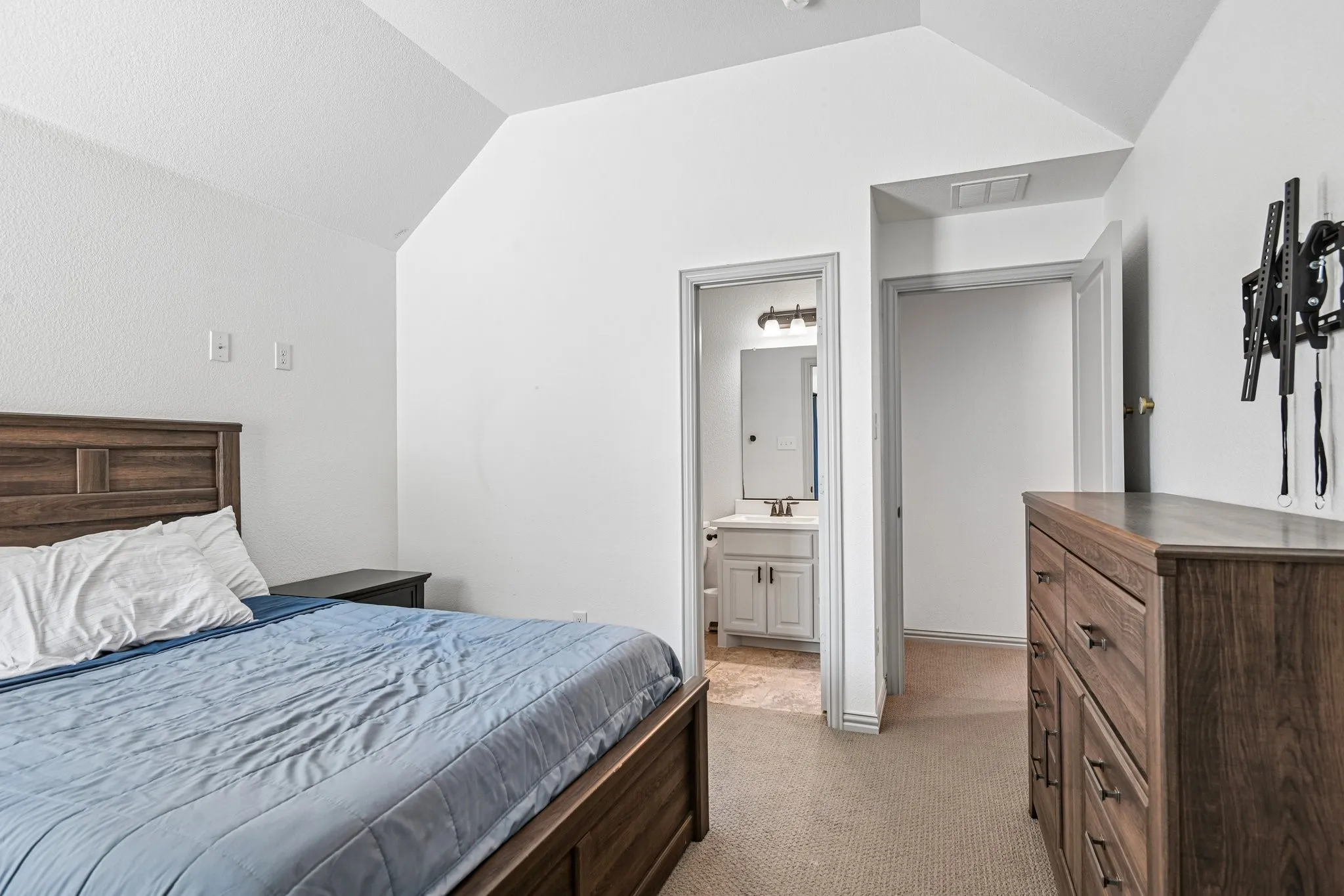 Carpeted room with a vaulted ceiling and an open doorway revealing a bathroom with a single vanity and mirrored medicine cabinet