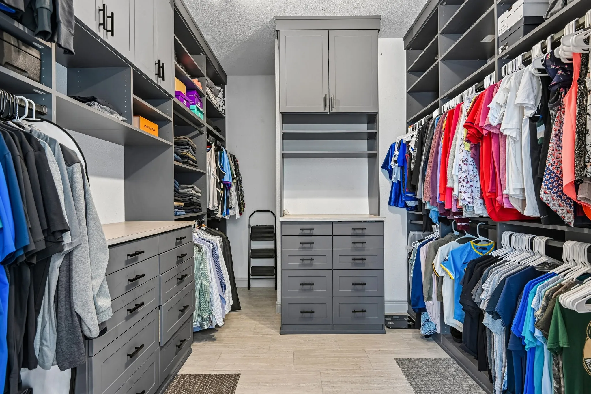 Master Custom built-in closet system featuring extensive shelving, hanging rods, central drawer island, additional cabinetry, and wood-finish flooring