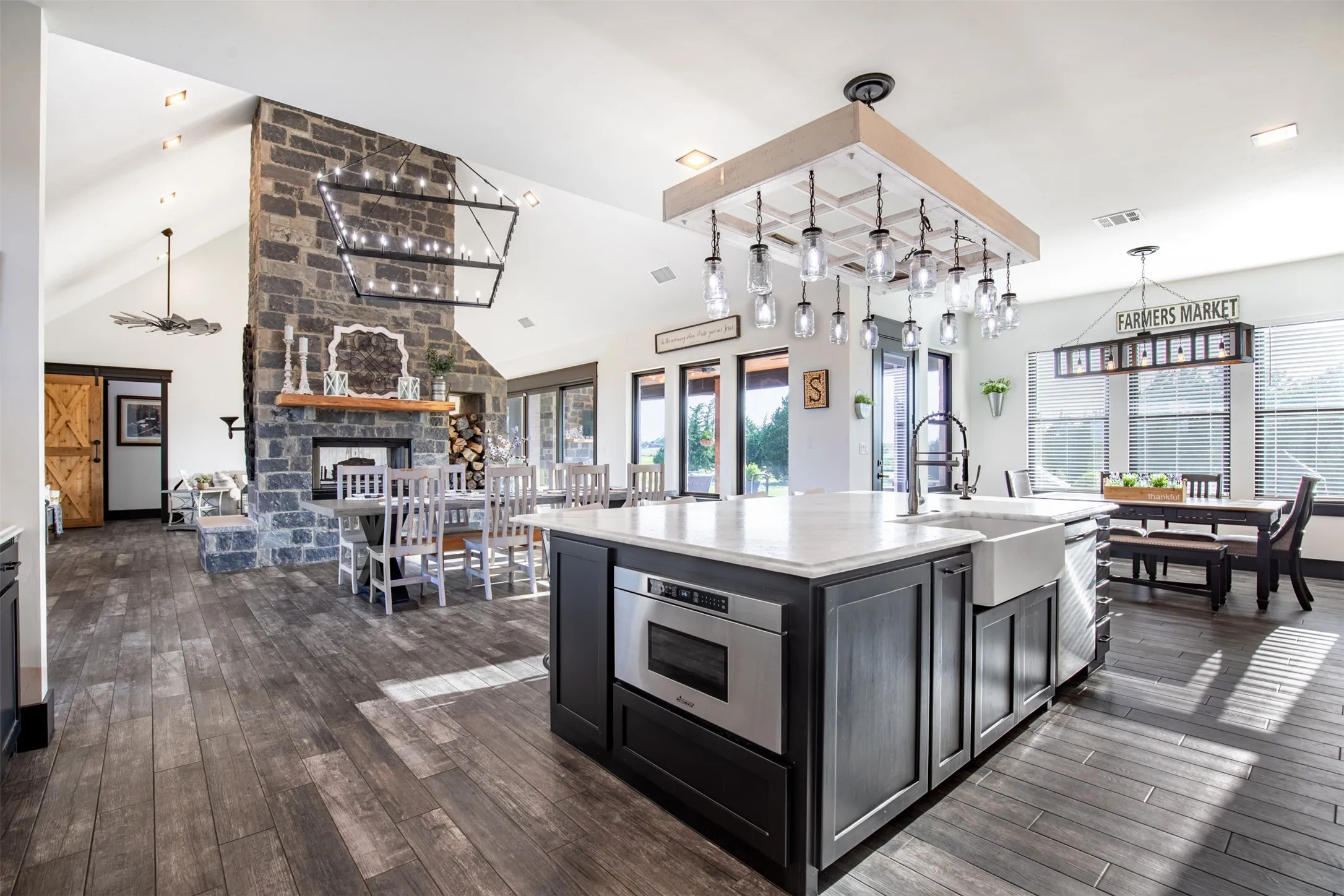 Spacious kitchen featuring a large island with an integrated microwave and farmhouse sink, built-in Kitchenaid cabinet, wood-finish flooring, and connectivity to dining areas