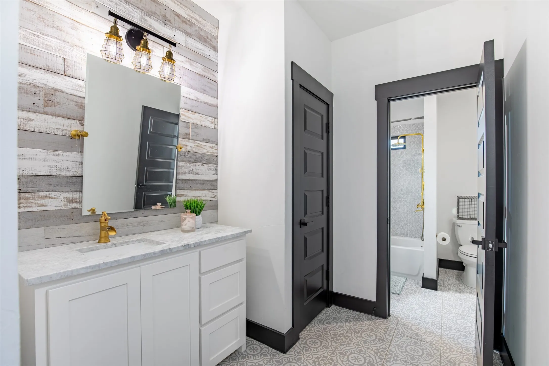 JnJ bathroom with brass fixtures, wood backsplash and decorative tile flooring