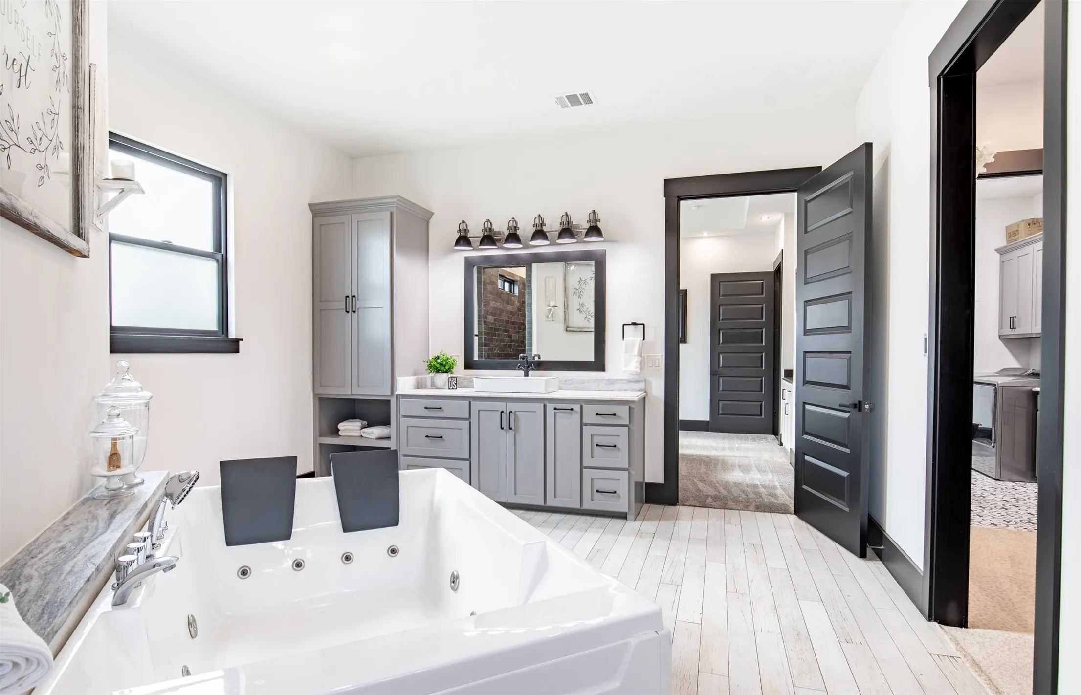 Spacious bathroom featuring a built-in two-person jetted tub, expansive grey cabinetry with ample storage, a dual vanities with a large mirrors, and private walk-in shower with dual heads