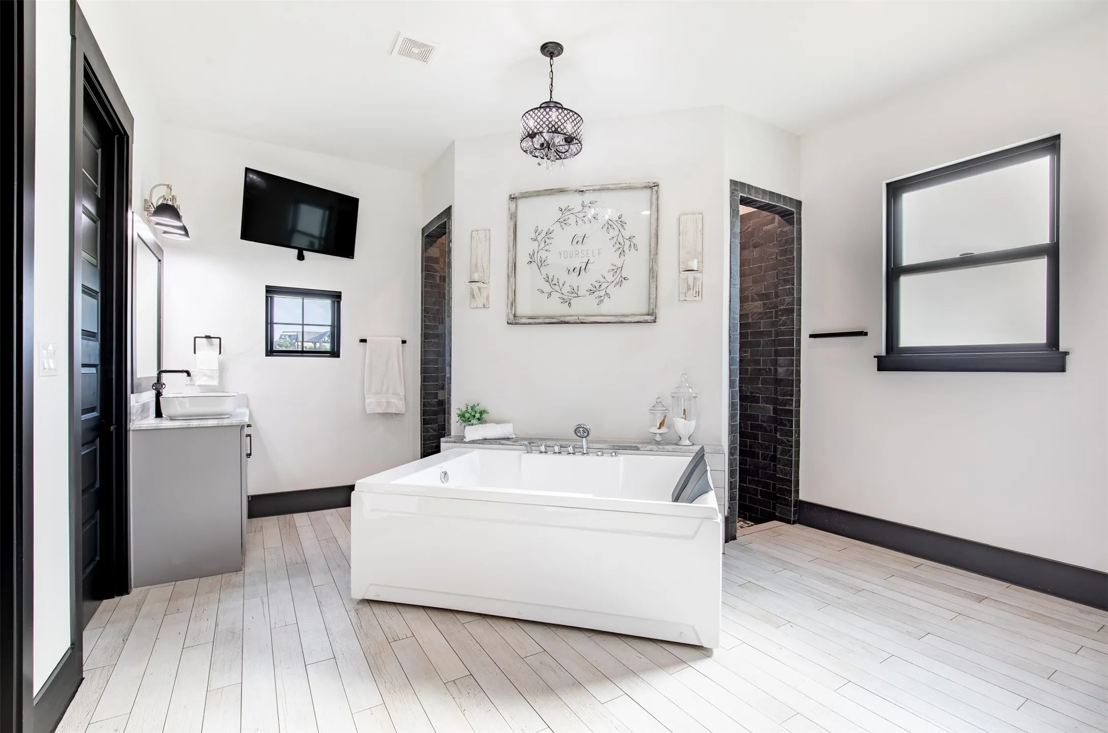 Freestanding two-person soaking tub centered in a spacious bathroom with double vanities and walk-in shower with double shower heads