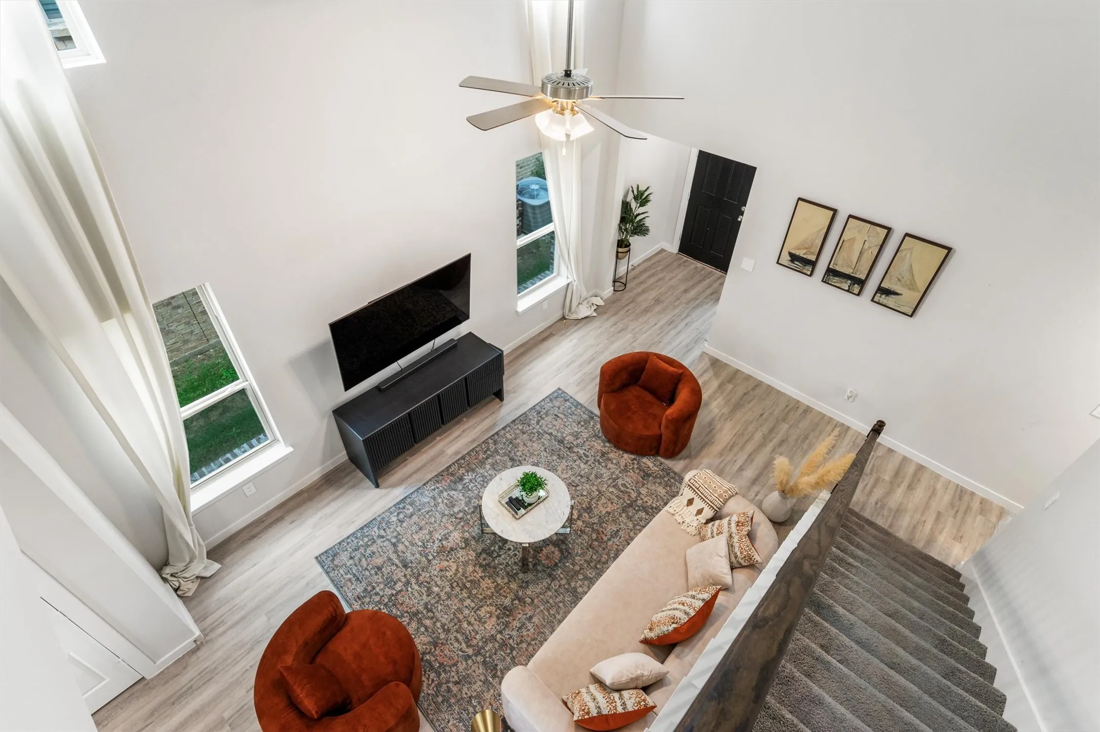 Living area with high ceilings, light wood-finish flooring, and multiple windows