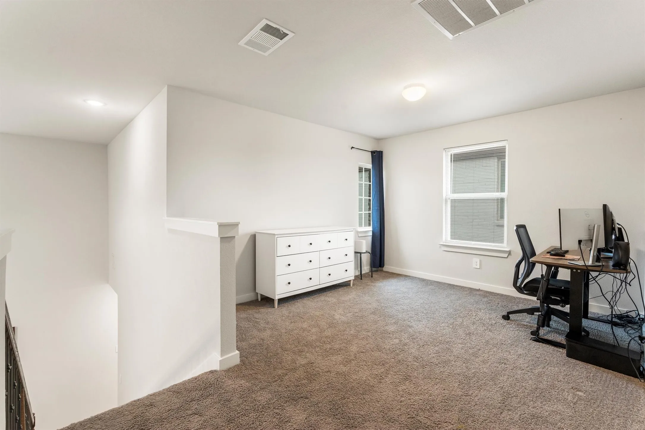 Carpeted loft area featuring a window with blue drapes, white walls, and a ceiling light fixture