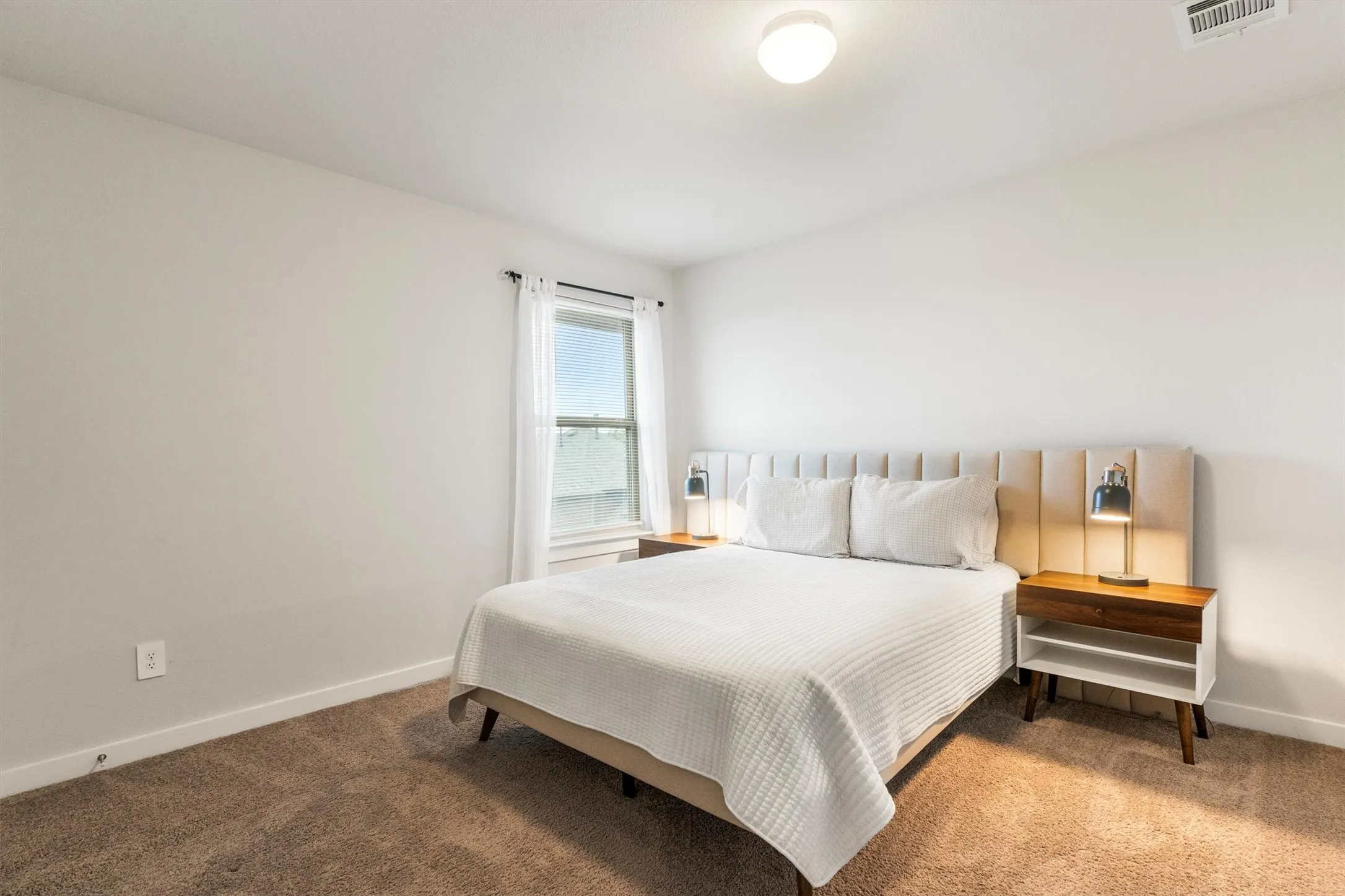 Carpeted bedroom featuring white walls, a ceiling-mounted light fixture, and a window with white trim