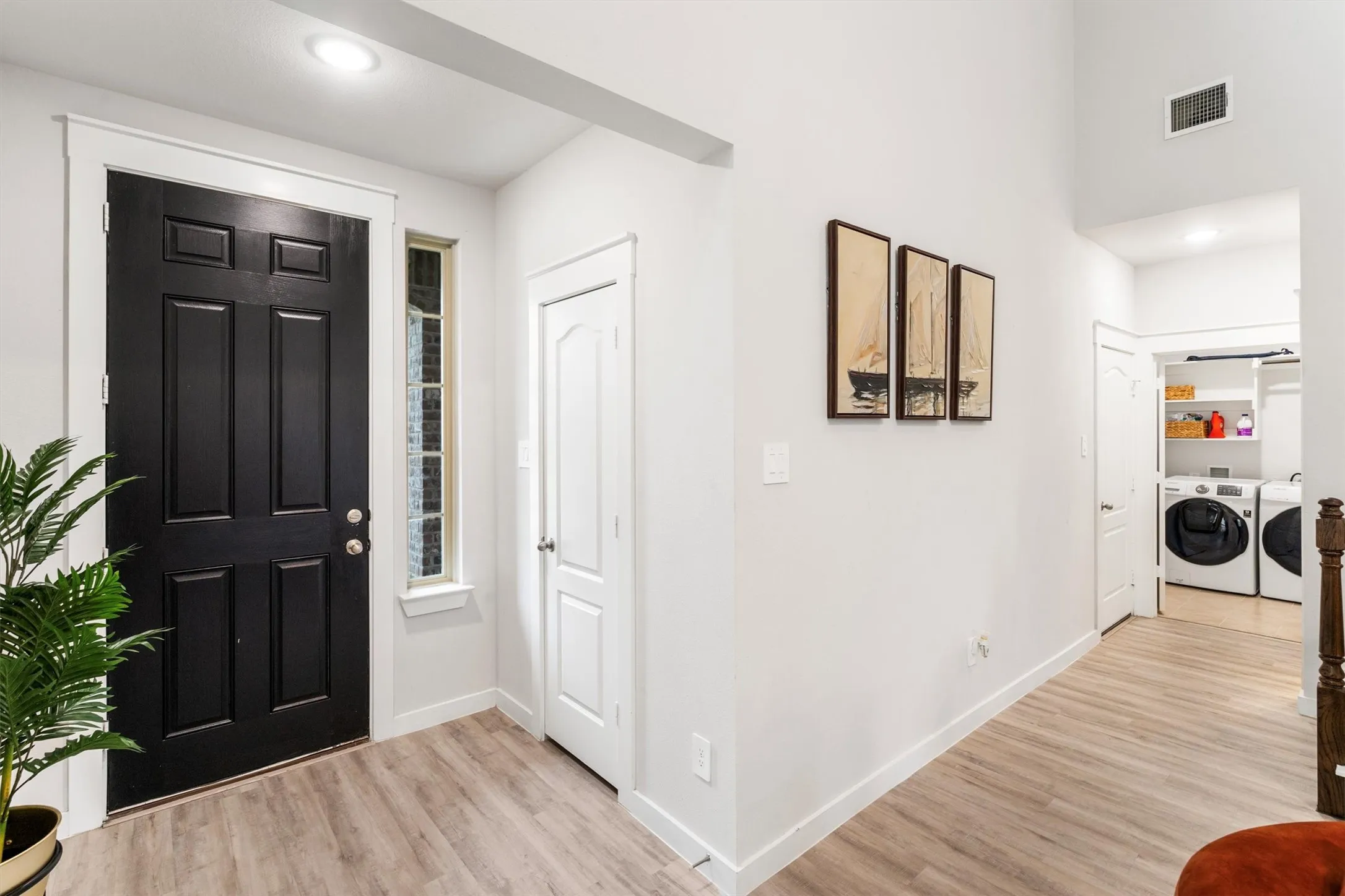 Entryway featuring a paneled black door with a sidelight, light wood-finish flooring, and white trim