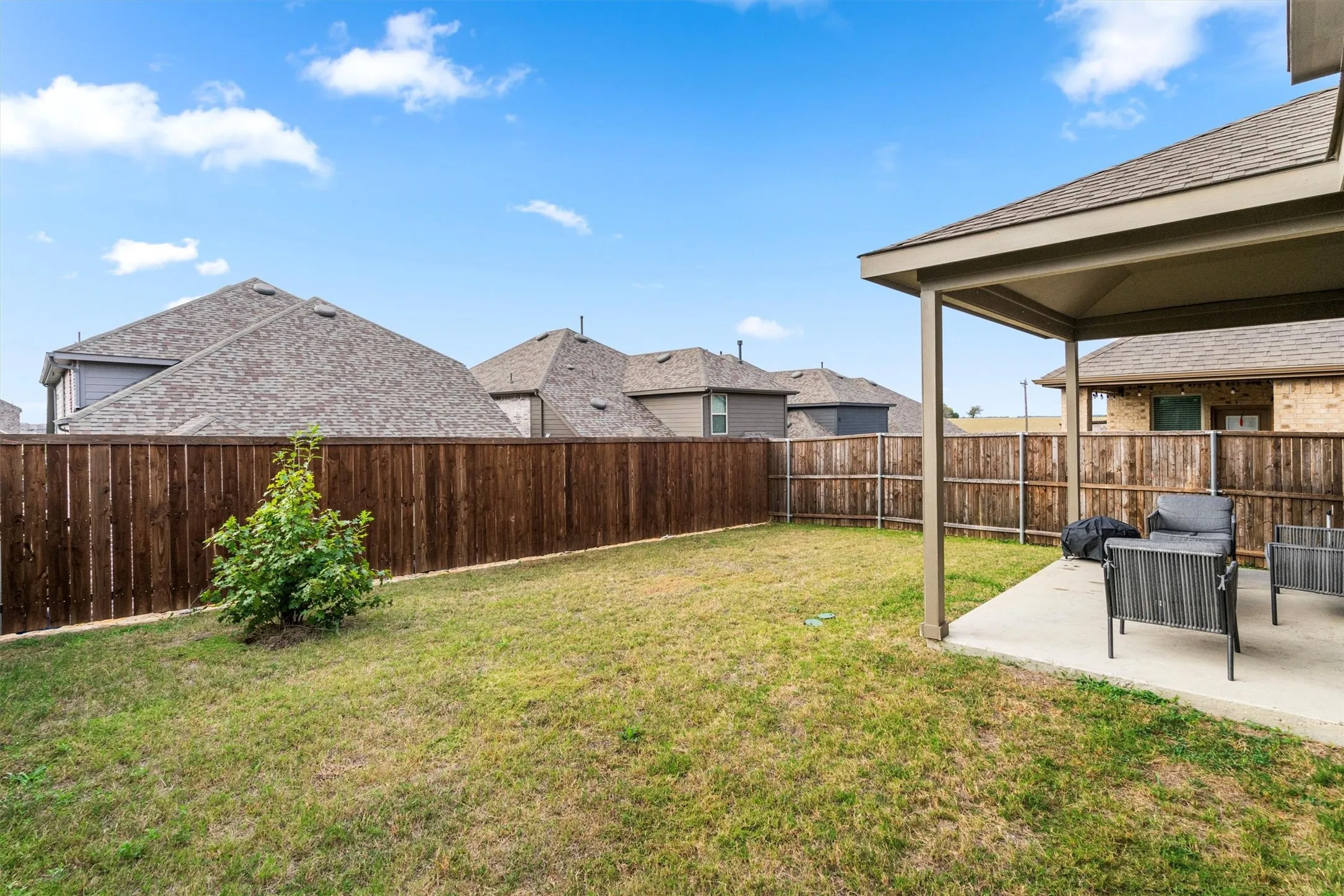 Expansive backyard featuring a covered patio with concrete flooring, a manicured lawn, and a privacy fence