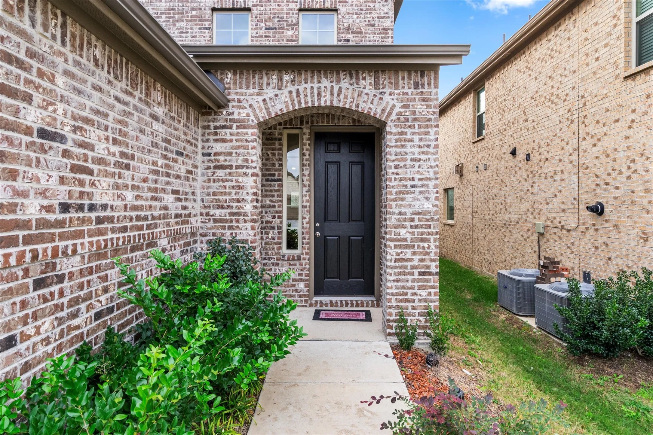 Brick facade with an arched entry, complemented by a paneled front door, side window, and mature landscaping
