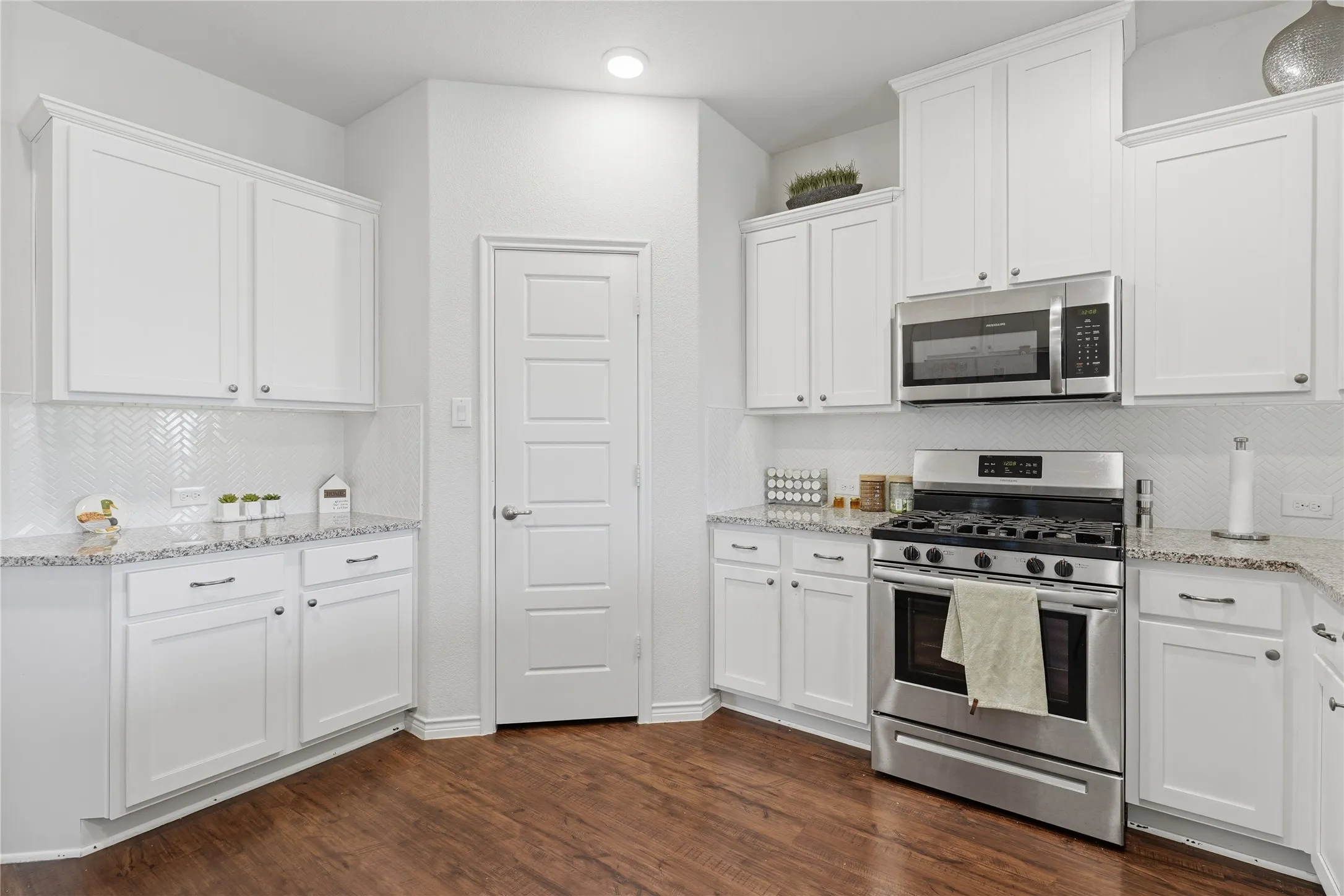 Spacious kitchen featuring white cabinetry, stone countertops, stainless steel appliances, a chevron-patterned tile backsplash, and wood-finish flooring