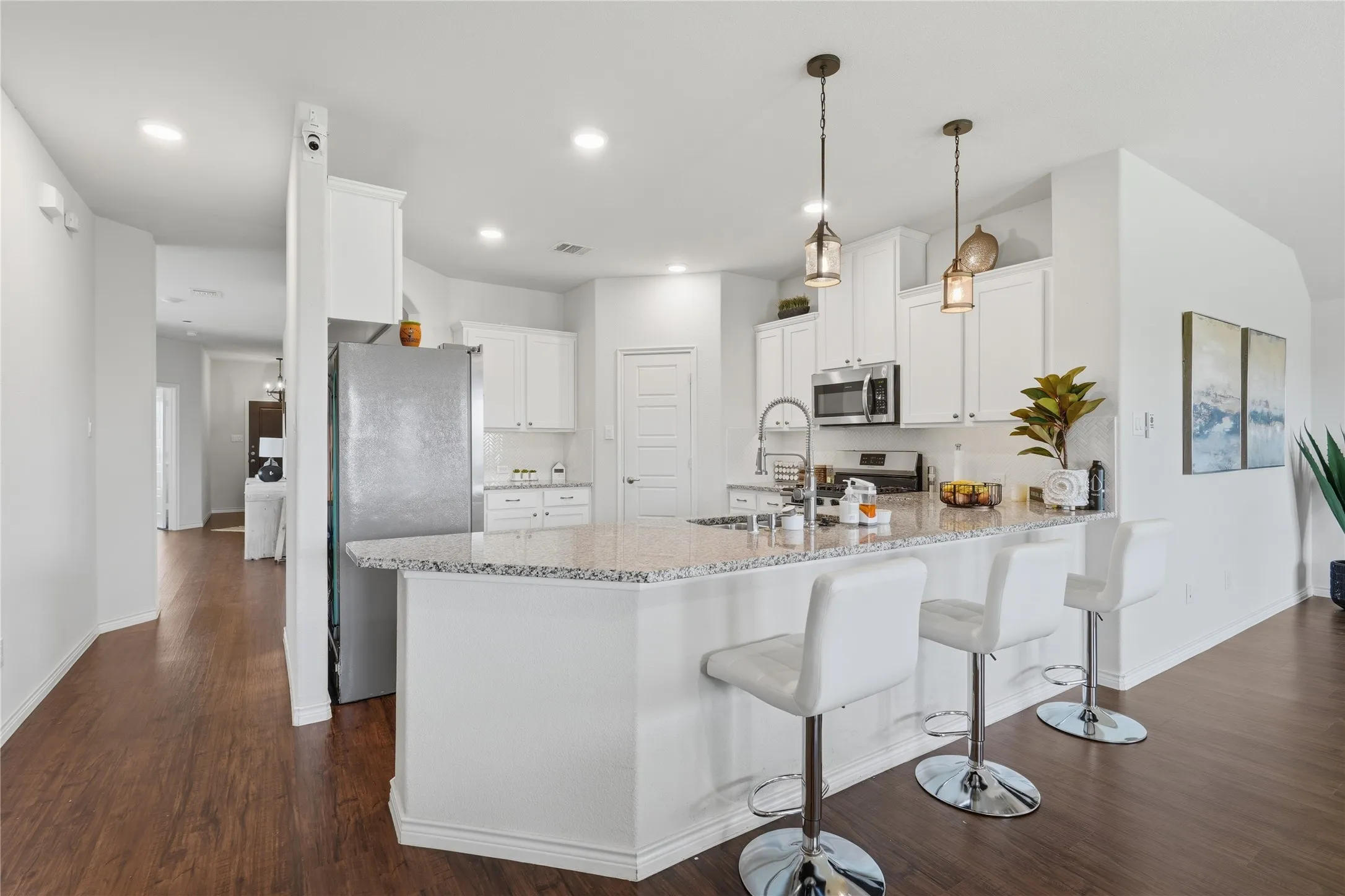 Kitchen featuring an expansive island with granite countertops, white cabinetry, stainless steel appliances, and two pendant lights