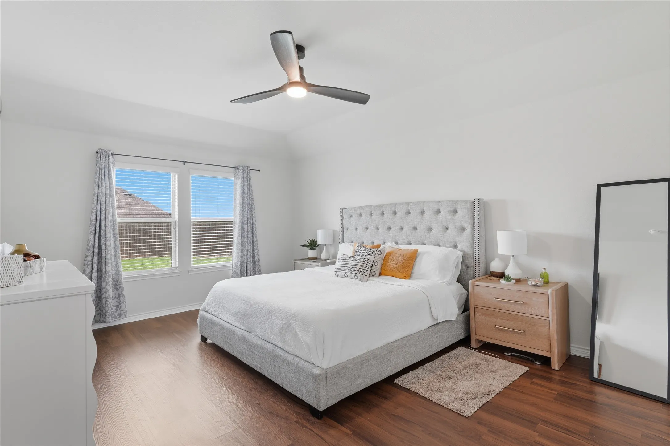 Spacious room featuring wood-finish flooring, a contemporary ceiling fan with integrated lighting, and dual windows with blinds