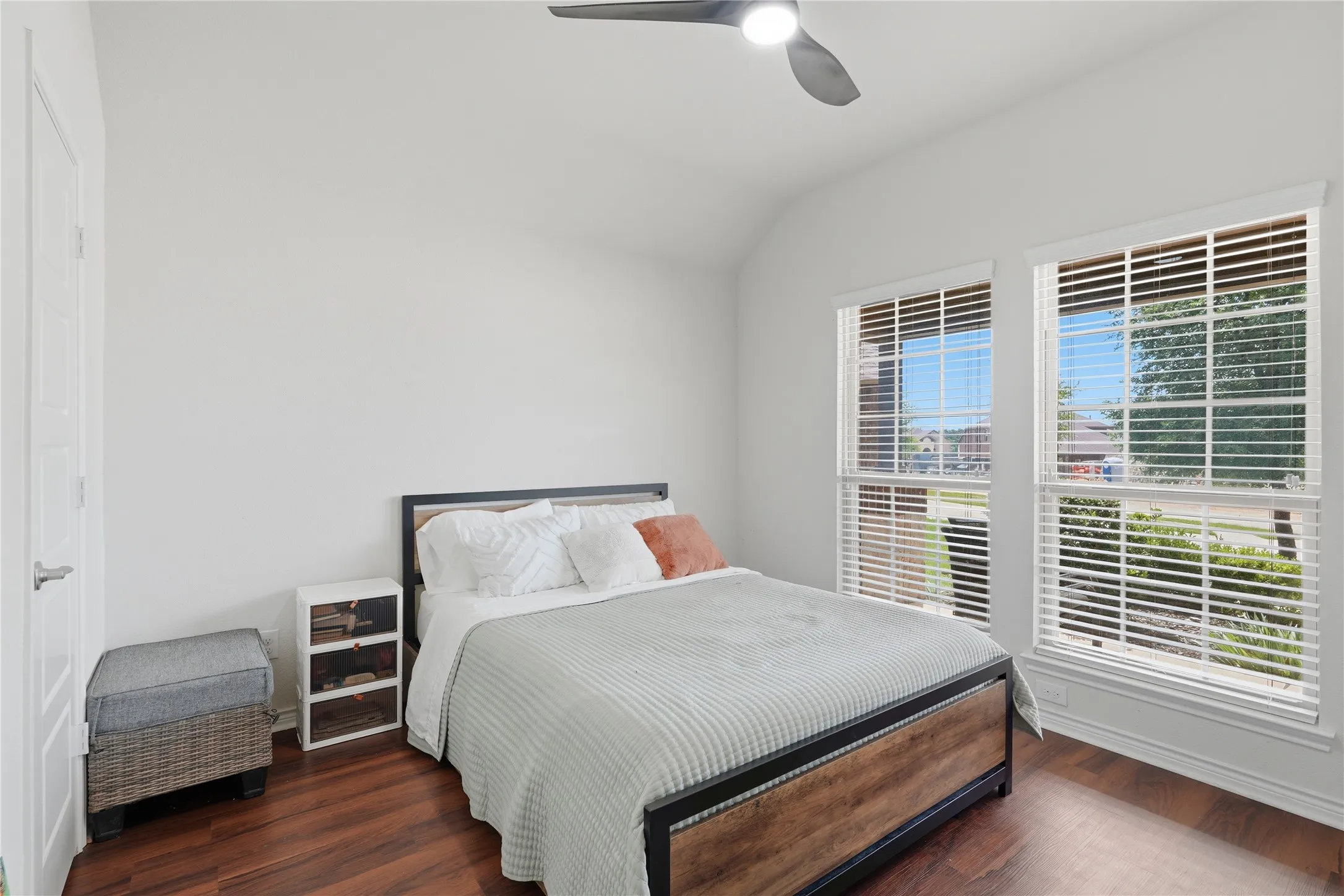 Room featuring wood-finish flooring, two large windows with blinds, a white door, and a ceiling fan with integrated lighting